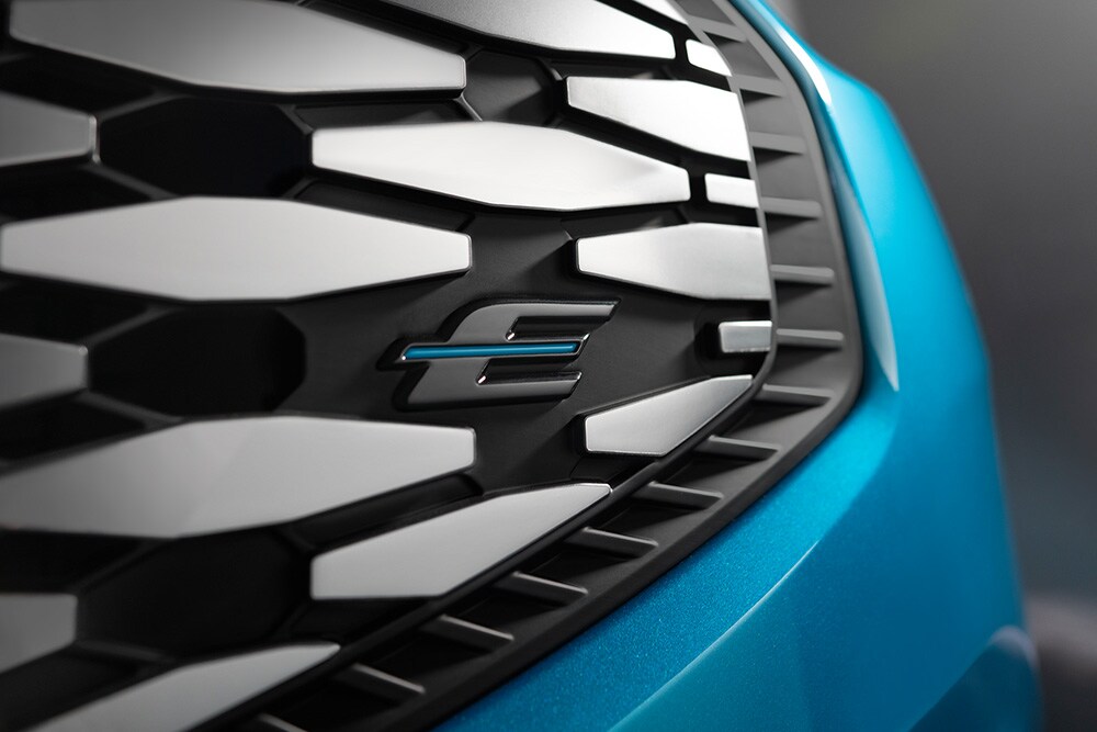 Gros plan sur la calandre du Ford E-Tourneo Custom avec le logo bleu « E », exclusif aux véhicules électriques Ford