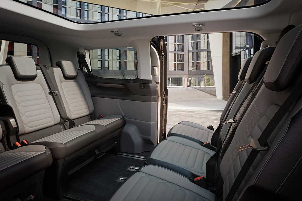 Vue intérieure du Ford Tourneo Custom avec plusieurs rangées de sièges gris et un toit panoramique