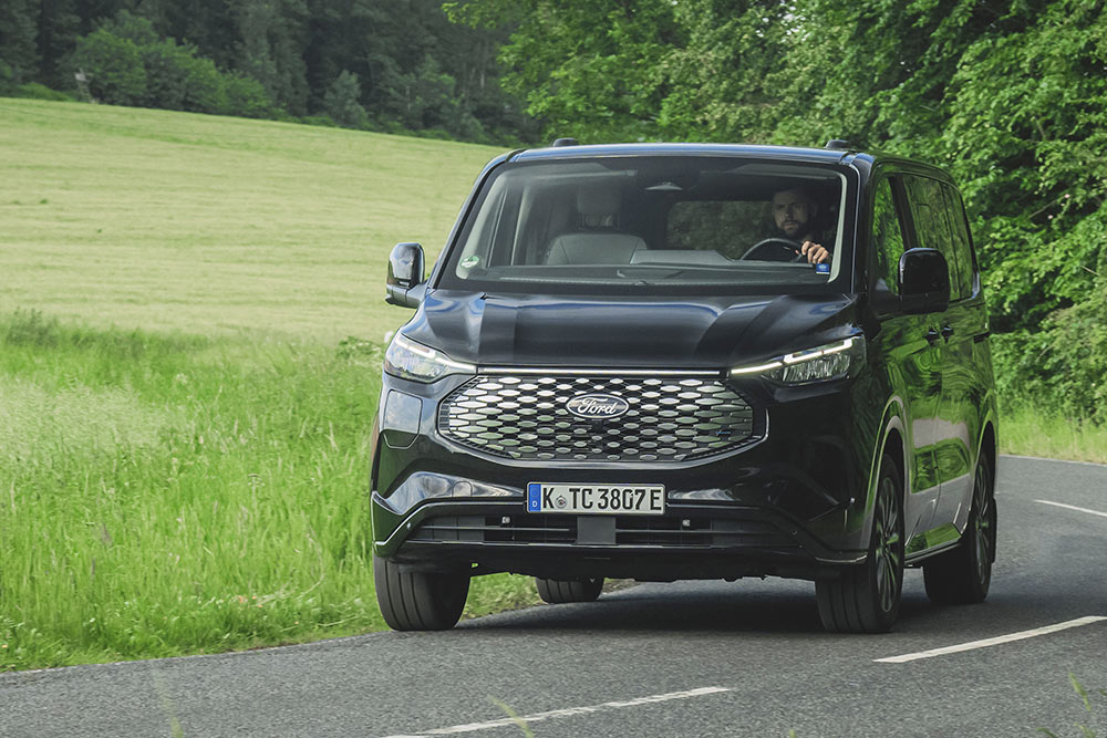 Ford E-Tourneo Custom noir roulant sur une route de campagne.