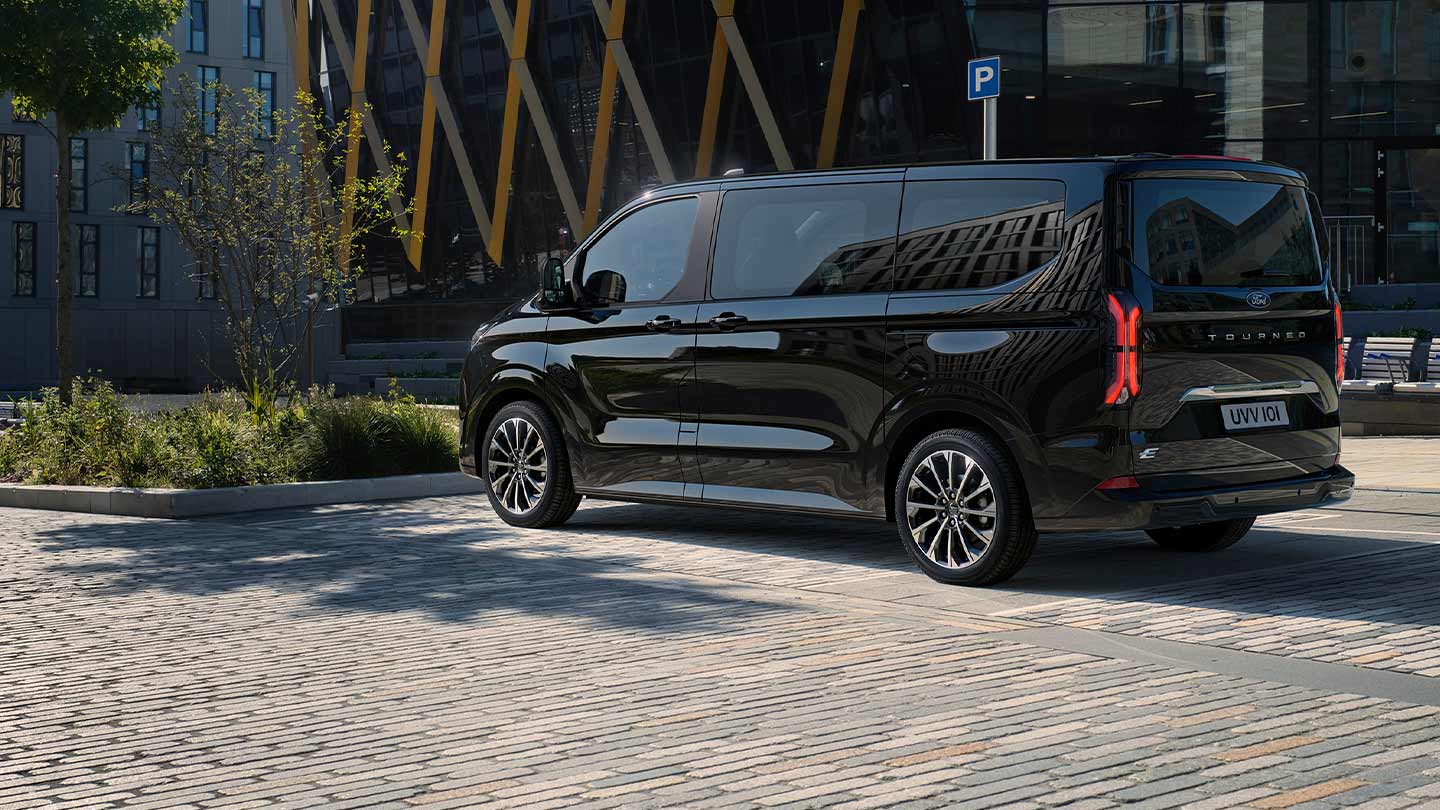 Ford E-Tourneo Custom noir, vue latérale et arrière devant un bâtiment moderne