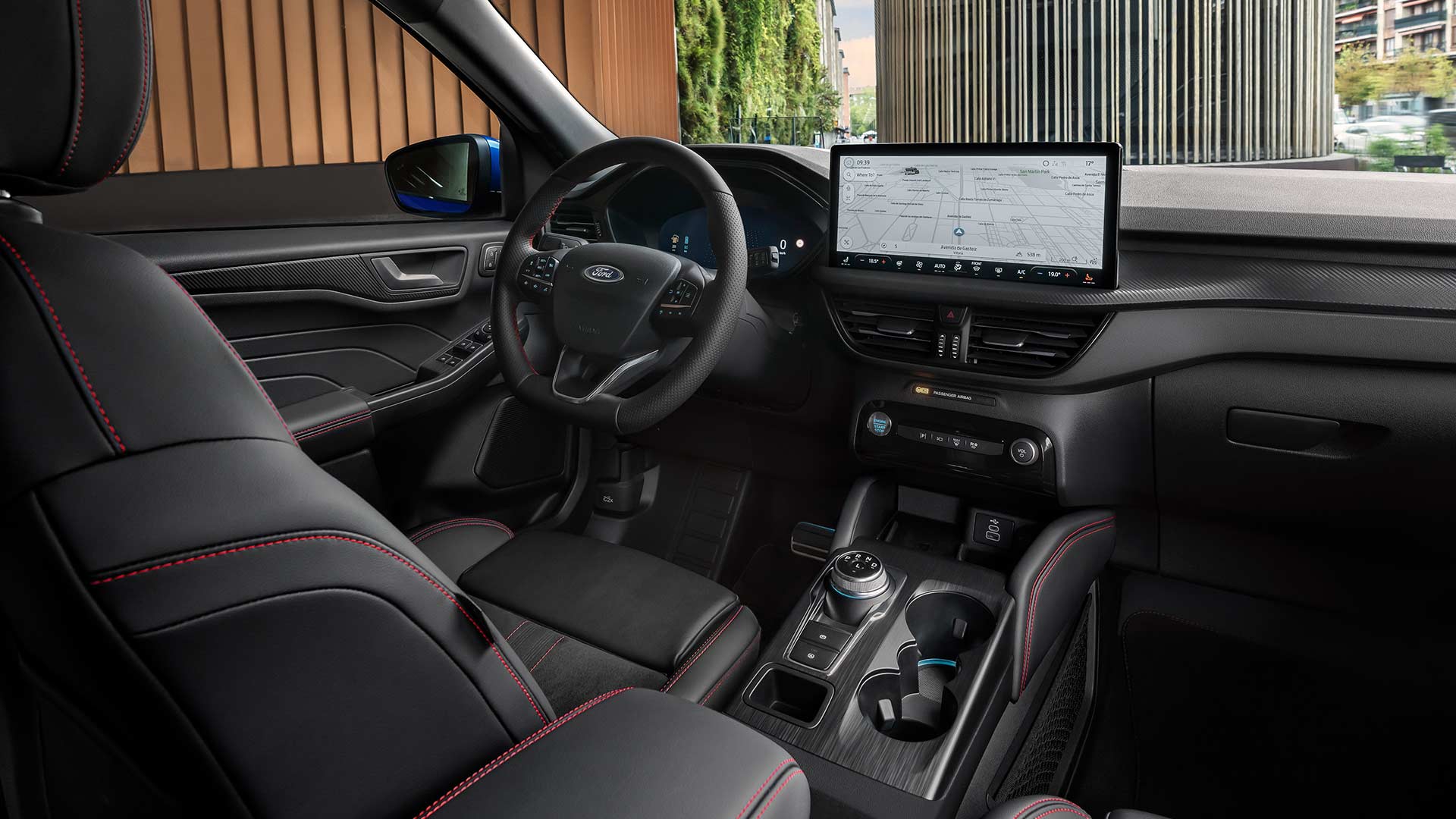 Intérieur du Ford Kuga avec logo Ford sur le volant, grand écran tactile SYNC® 4 et sièges noirs avec surpiqûres rouges.