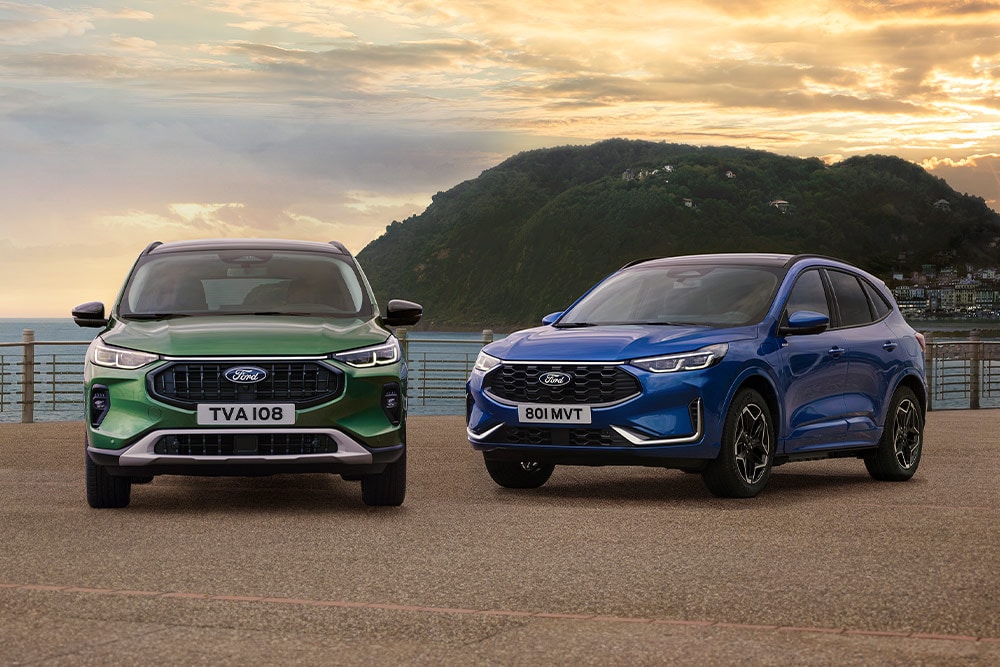 Un Ford Kuga Active de couleur verte et un Ford Kuga ST Line de couleur bleue garés côte à côte sur un parking côtier.
