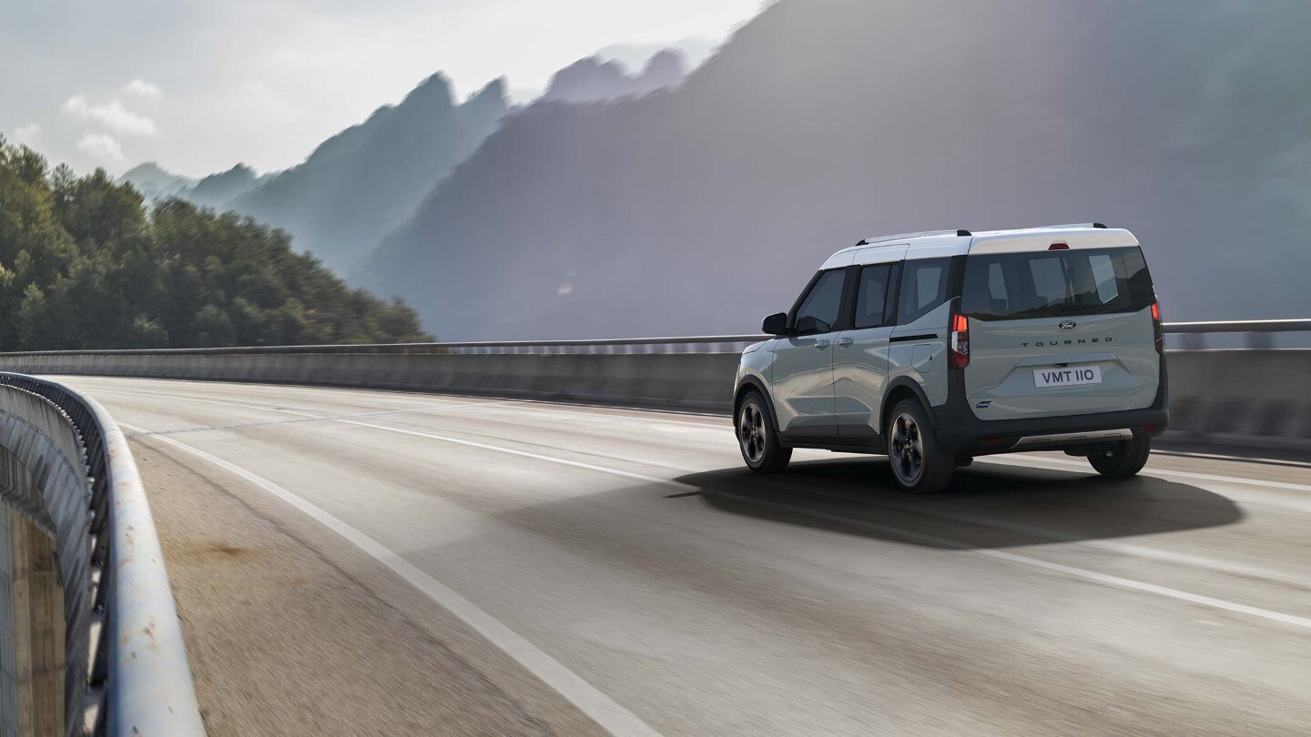 Ford Tourneo Courier couleur grise, vue arrière aux trois quarts, roulant sur un pont