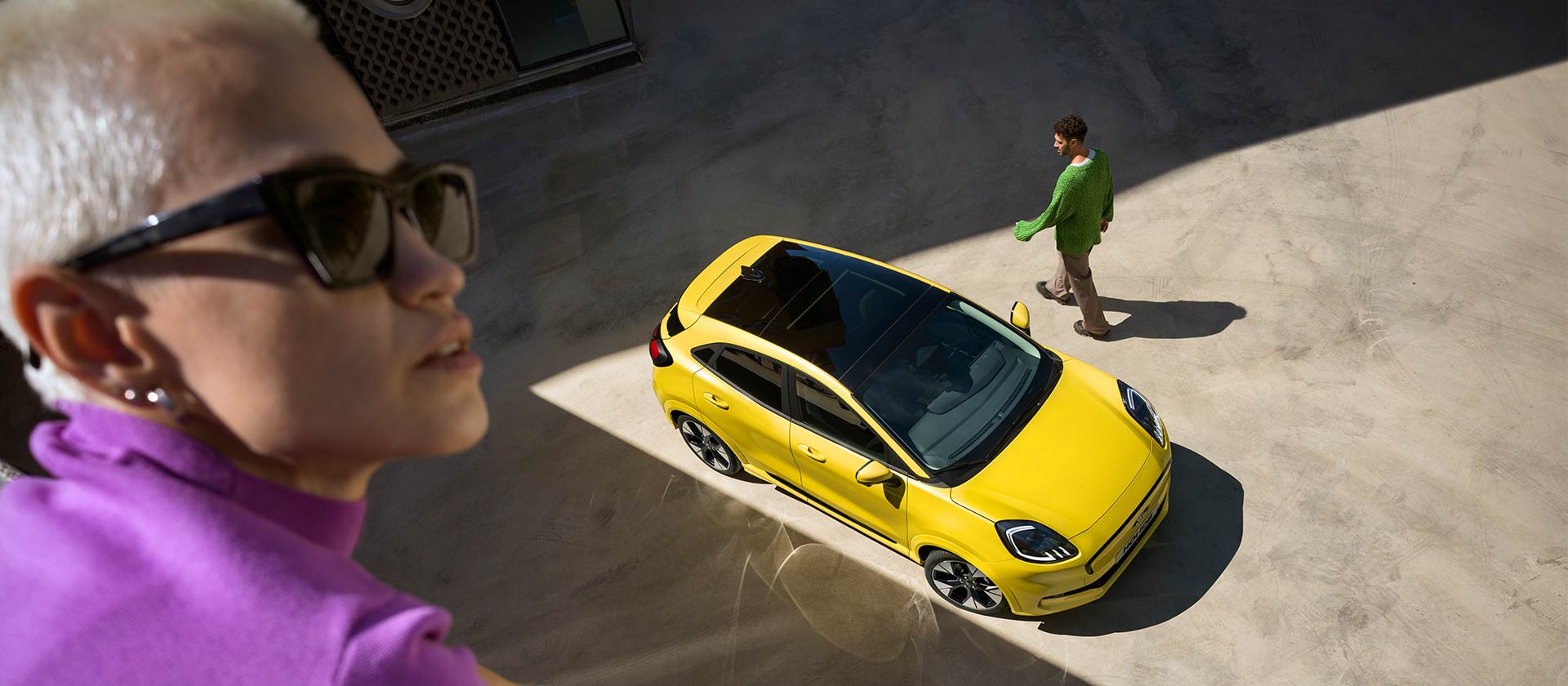 Vue du dessus d’une Ford Puma Gen-E® électrique jaune. Personne en violet au premier plan.