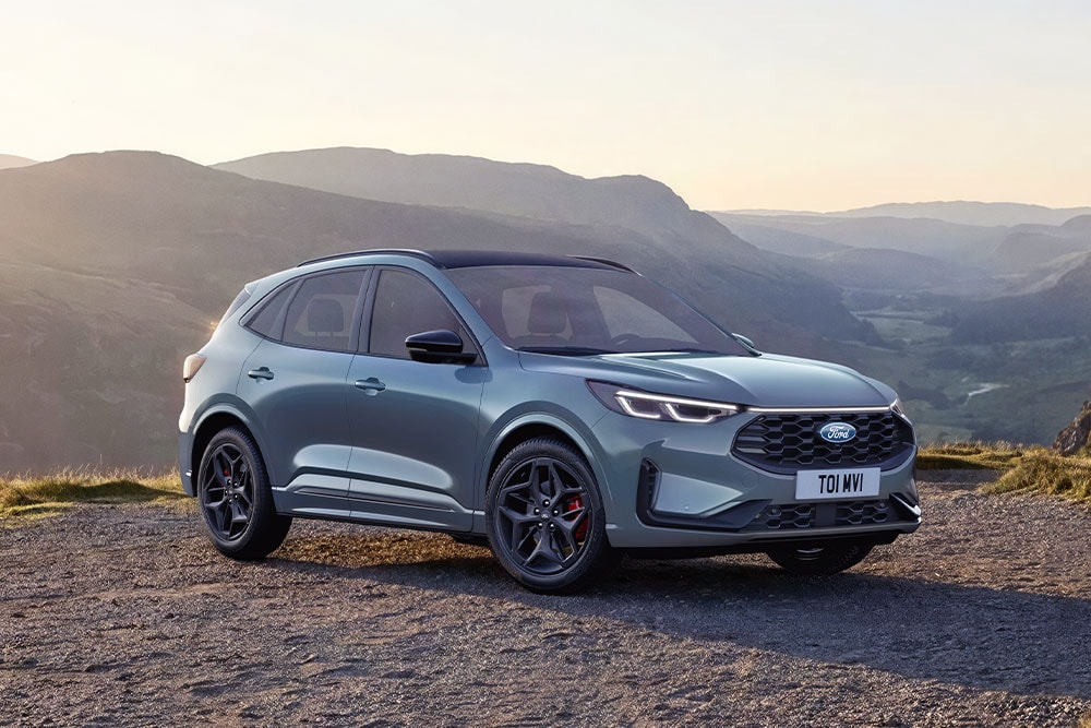 Un Ford Kuga gris est garé sur un chemin de gravier au coucher du soleil.