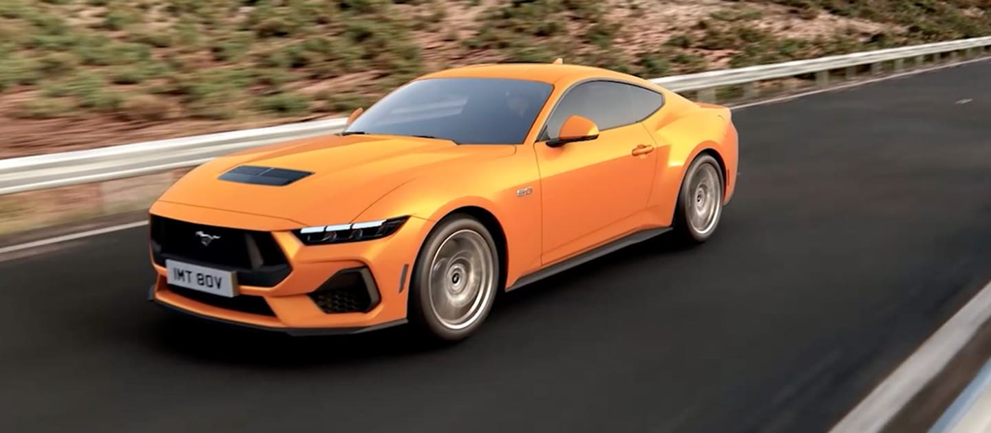 A Ford Mustang GT Fastback in Orange Fury paint driving along a mountain road.