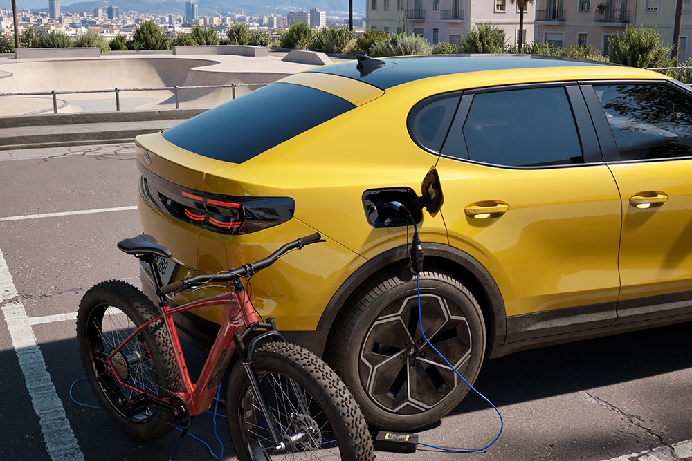 Une Ford Capri® jaune garée, chargeant un vélo électrique rouge dans un paysage urbain.