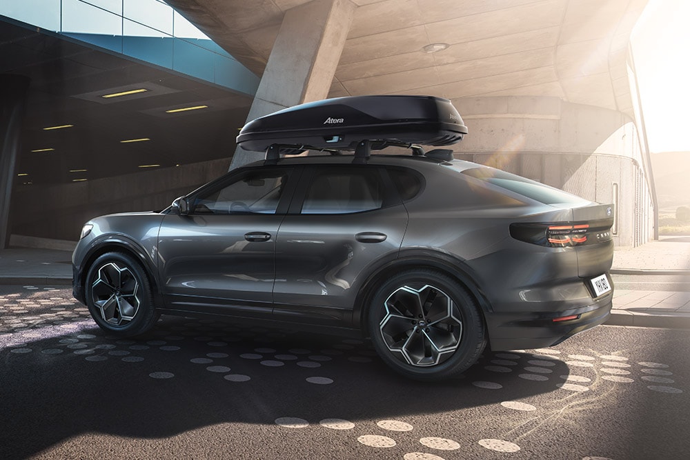 Vue 3/4 latérale d'une Ford Capri rouge avec coffre de toit, garée sous une structure de bâtiment moderne.