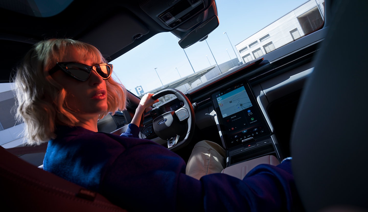 Une femme est assise sur le siège du conducteur d’une Ford Capri® stationnée, volant et grand écran tactile SYNC® Move visibles.