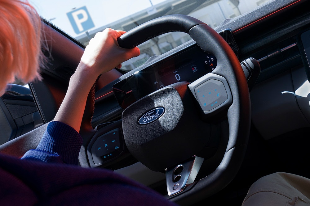 Gros plan sur une femme tenant le volant d’une Ford Capri stationnée, montrant également le combiné d’instruments numérique.