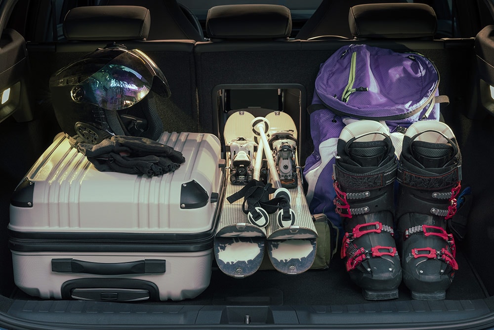 Le compartiment à bagages arrière du Ford Explorer contenant une valise blanche et un équipement de ski installé via la trappe. 