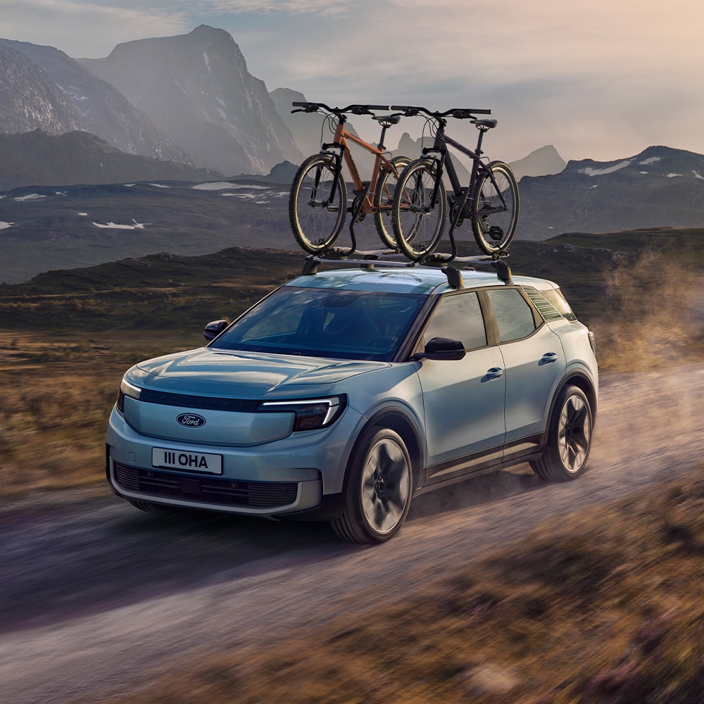 Ford Explorer de couleur bleue circulant sur un chemin de terre, avec barres de toit, porte-vélos et deux vélos montés sur le toit.