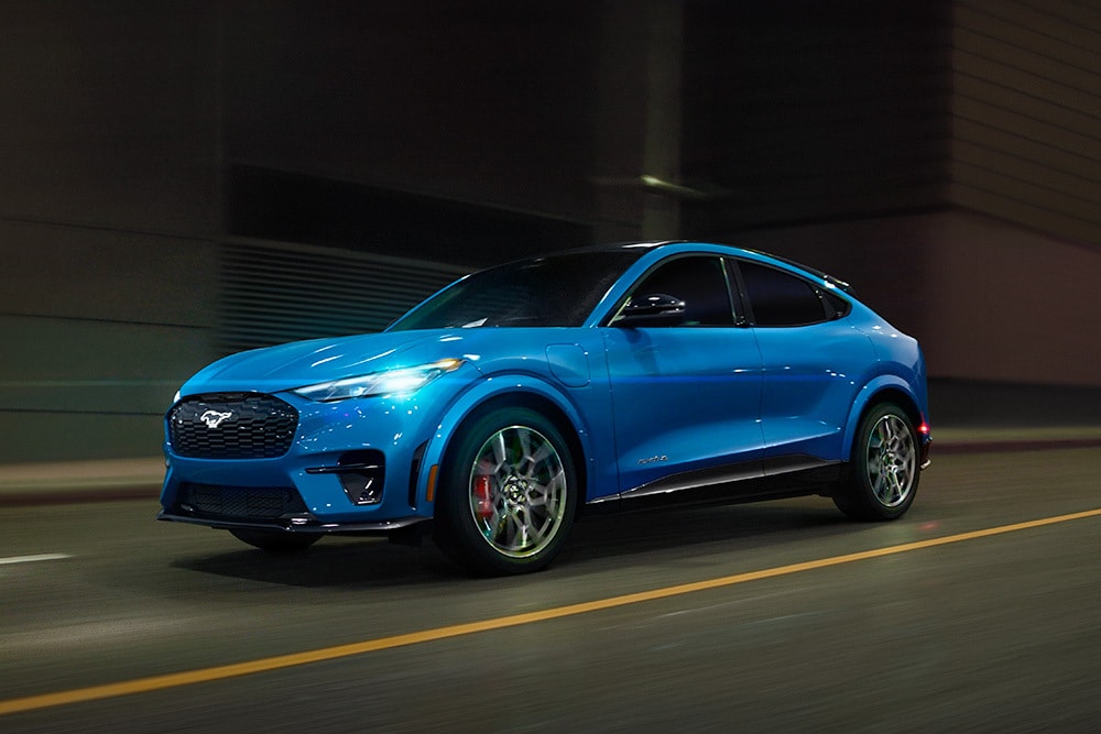 Une voiture de sport électrique Ford Mustang Mach-E GT bleue circulant sur une route ouverte.