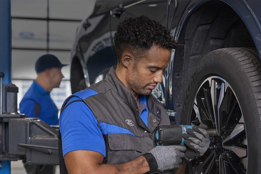 Un technicien Ford utilise une clé à chocs sur une roue, un collègue travaillant derrière.