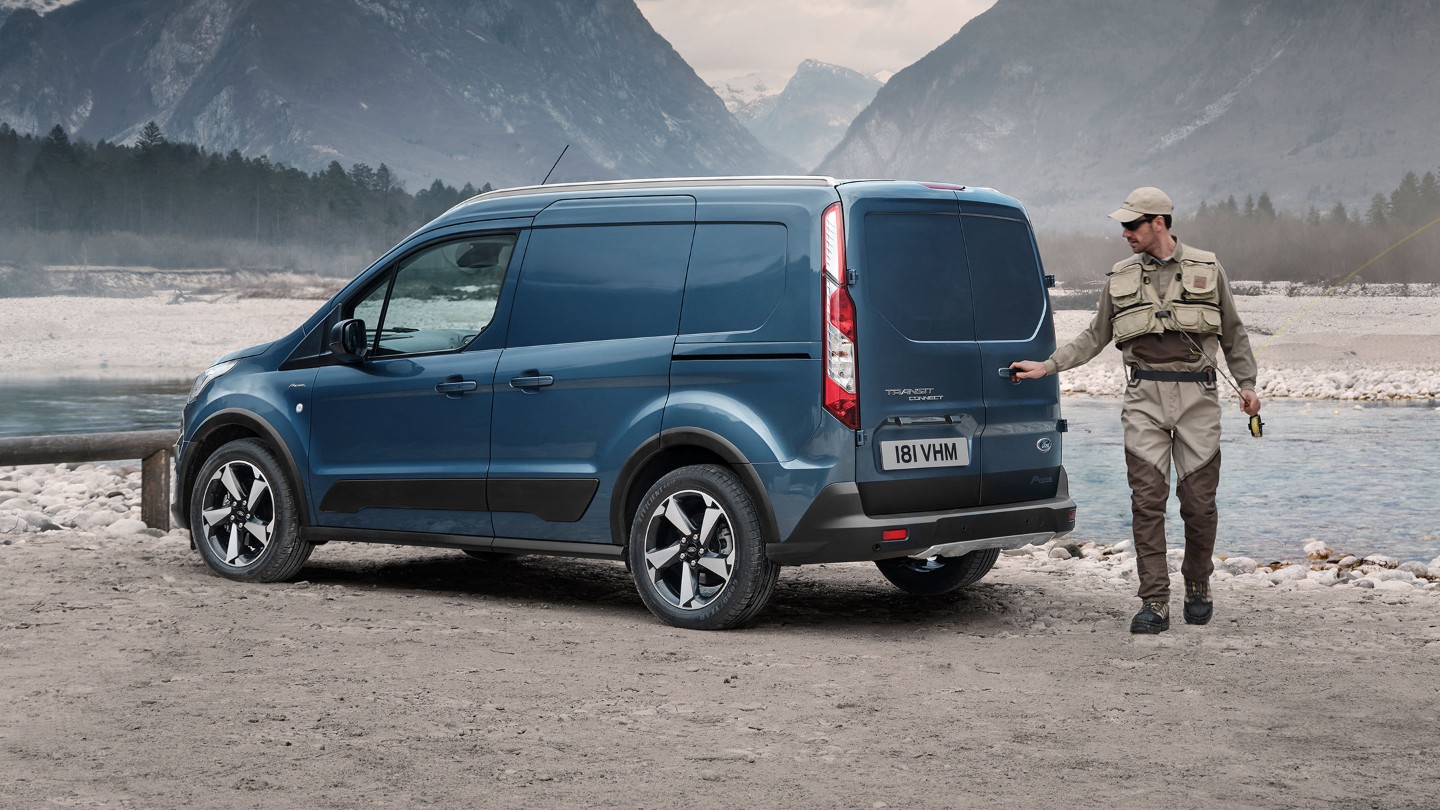 Ford Transit Connect Active bleu, vue latérale aux trois quarts, garé le long d’une rivière de montagne, avec pêcheur