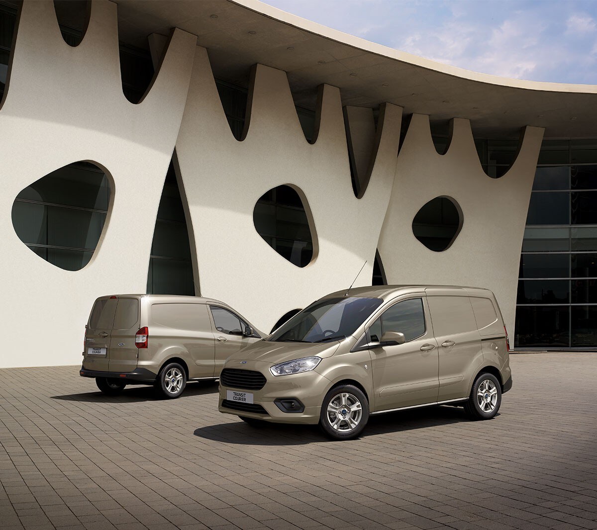 Ford Transit Courier en champagne, respectivement en vue avant et arrière ¾ se garent l'un devant l'autre.