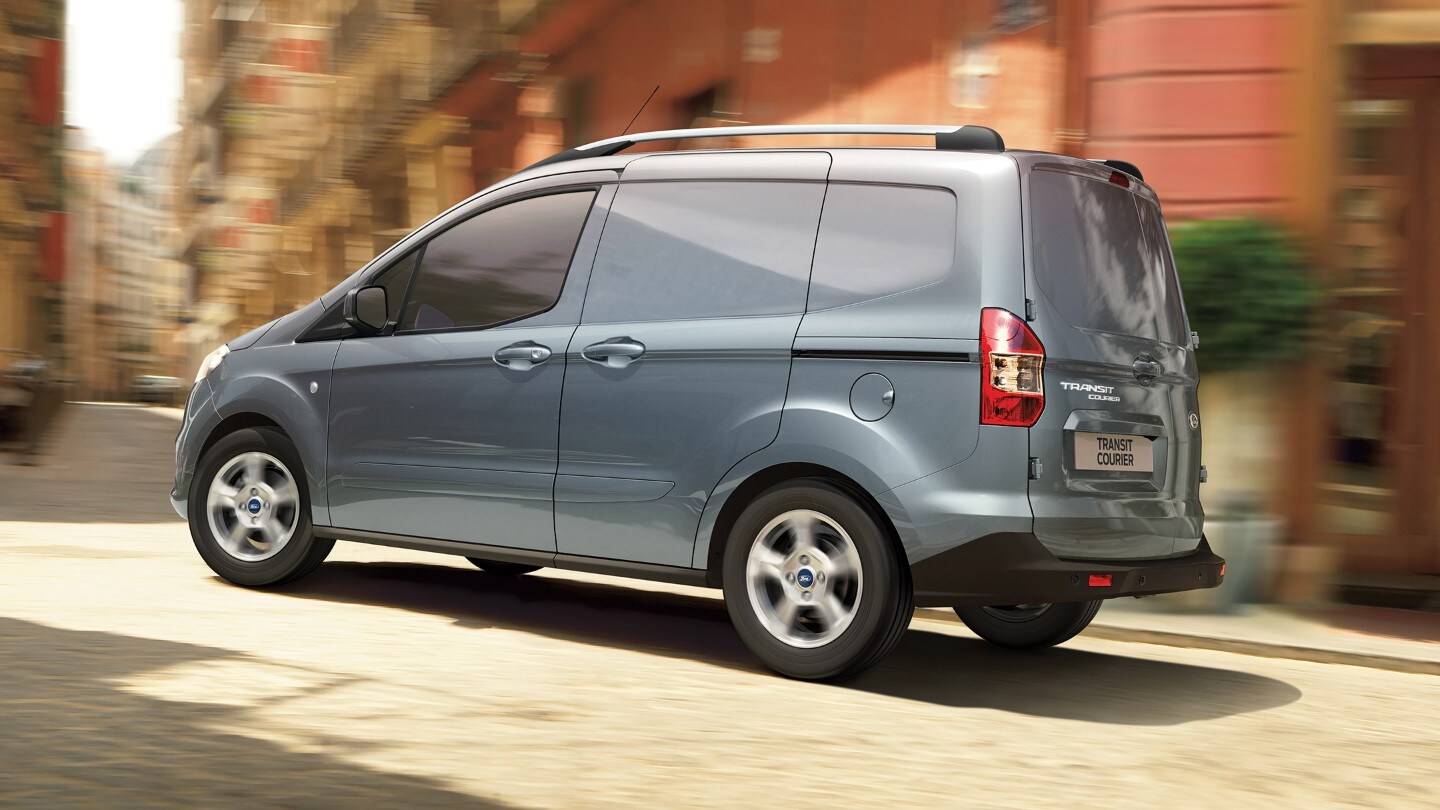 Ford Transit Courier couleur grise, vue latérale, roulant dans des rues étroites d’un centre-ville