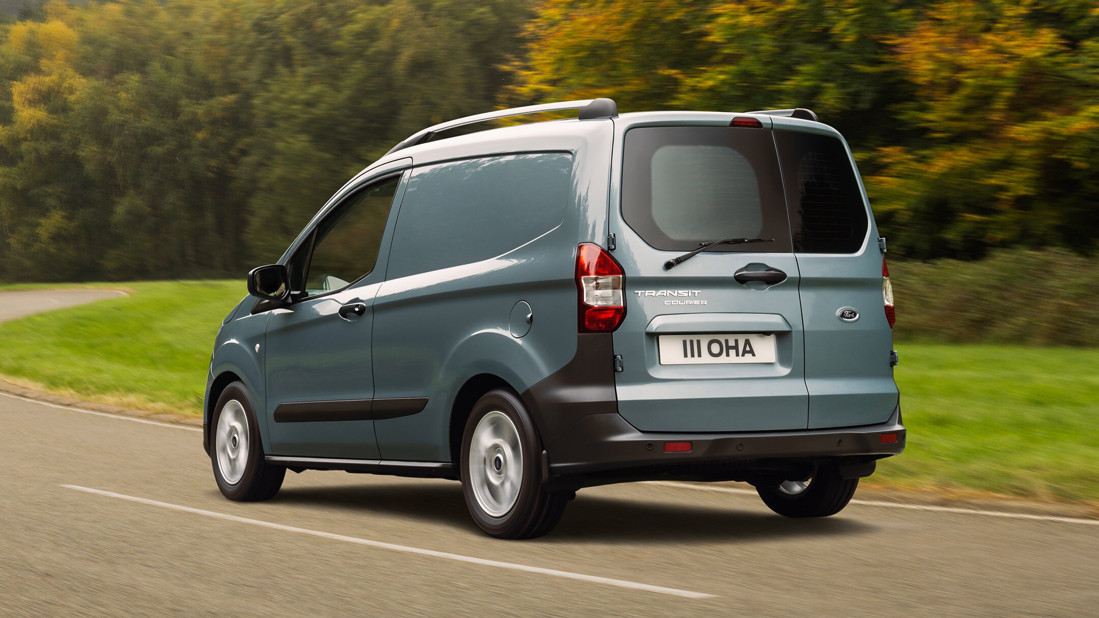 Ford Transit Connect couleur grise, vue arrière aux trois quarts, roulant sur une route de campagne