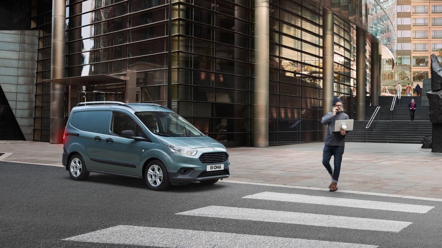 Ford Transit Courier couleur grise, vue latérale, s’arrêtant devant un passage piéton dans un centre-ville