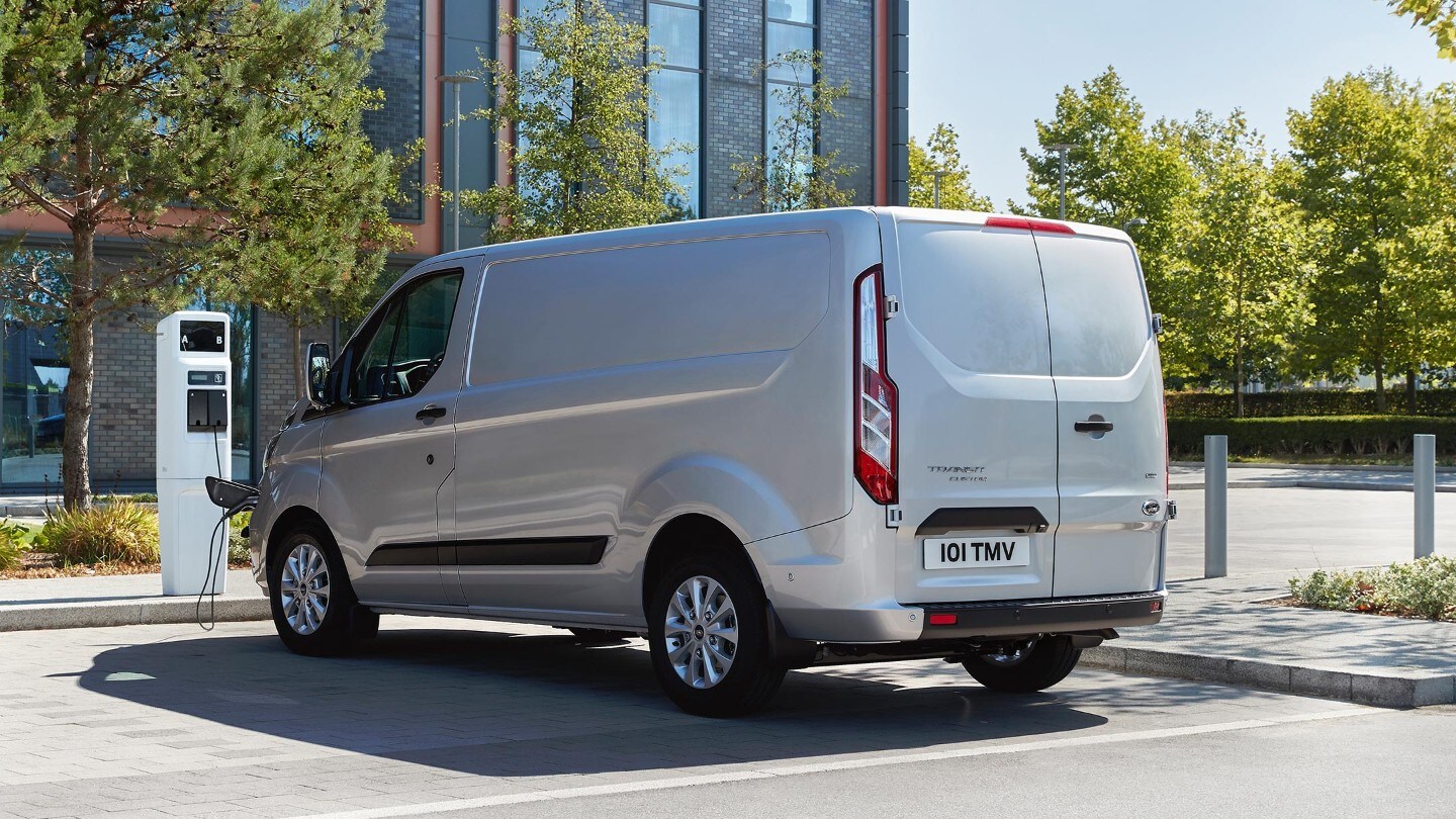 Ford Transit Custom Plug-In Hybrid couleur argent, vue arrière aux trois quarts, charge à une station de recharge