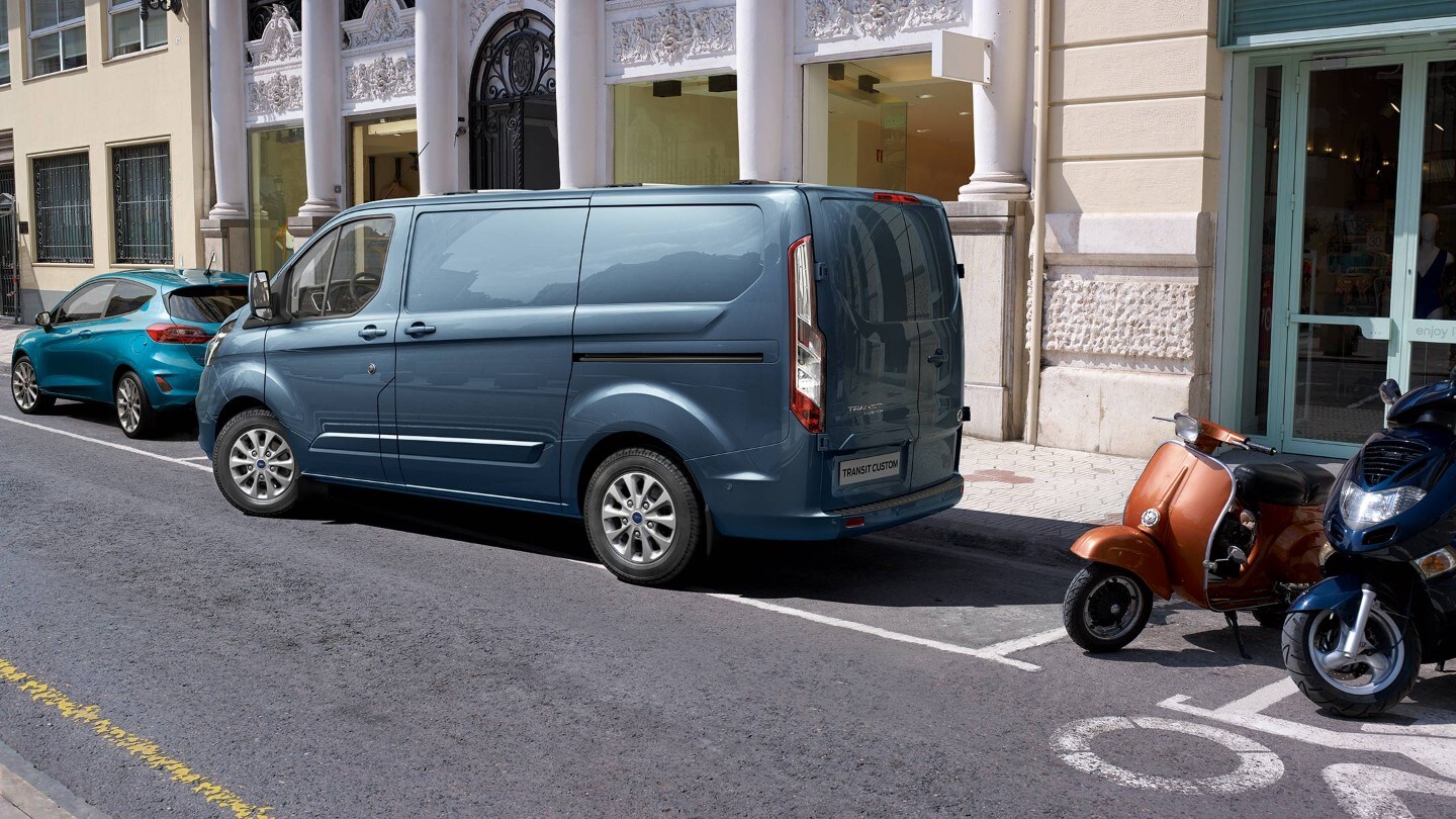 Ford Transit Custom couleur bleue, vue arrière aux trois quarts, se garant en marche arrière dans une place de parc