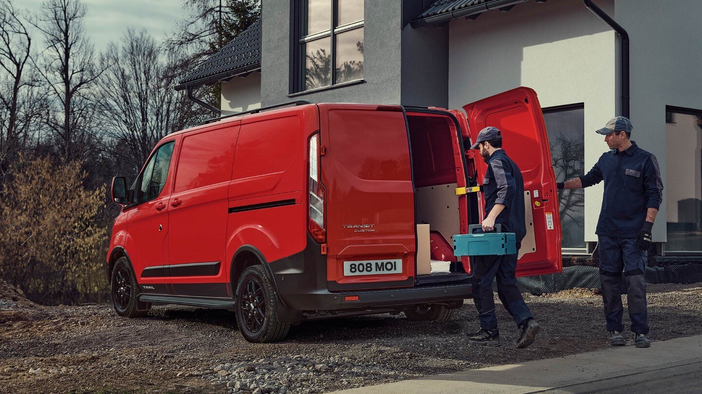 Ford Transit Custom Trail rouge, vue latérale aux trois quarts, se gare dans la zone de développement et est chargé 