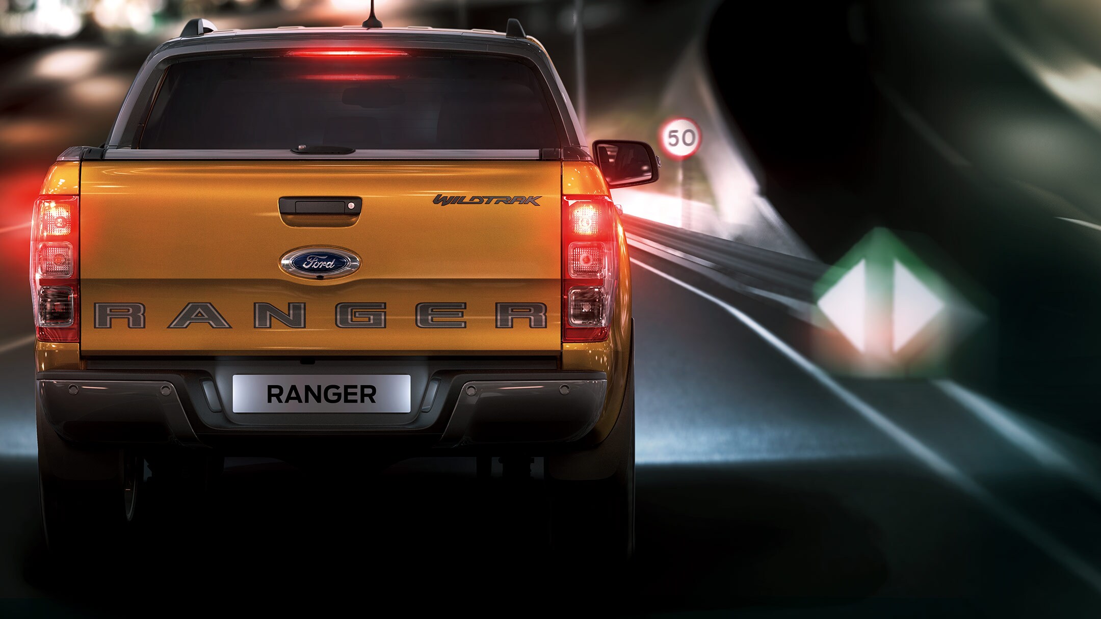 Ford Ranger couleur orange, vue arrière, roulant sur une route de nuit