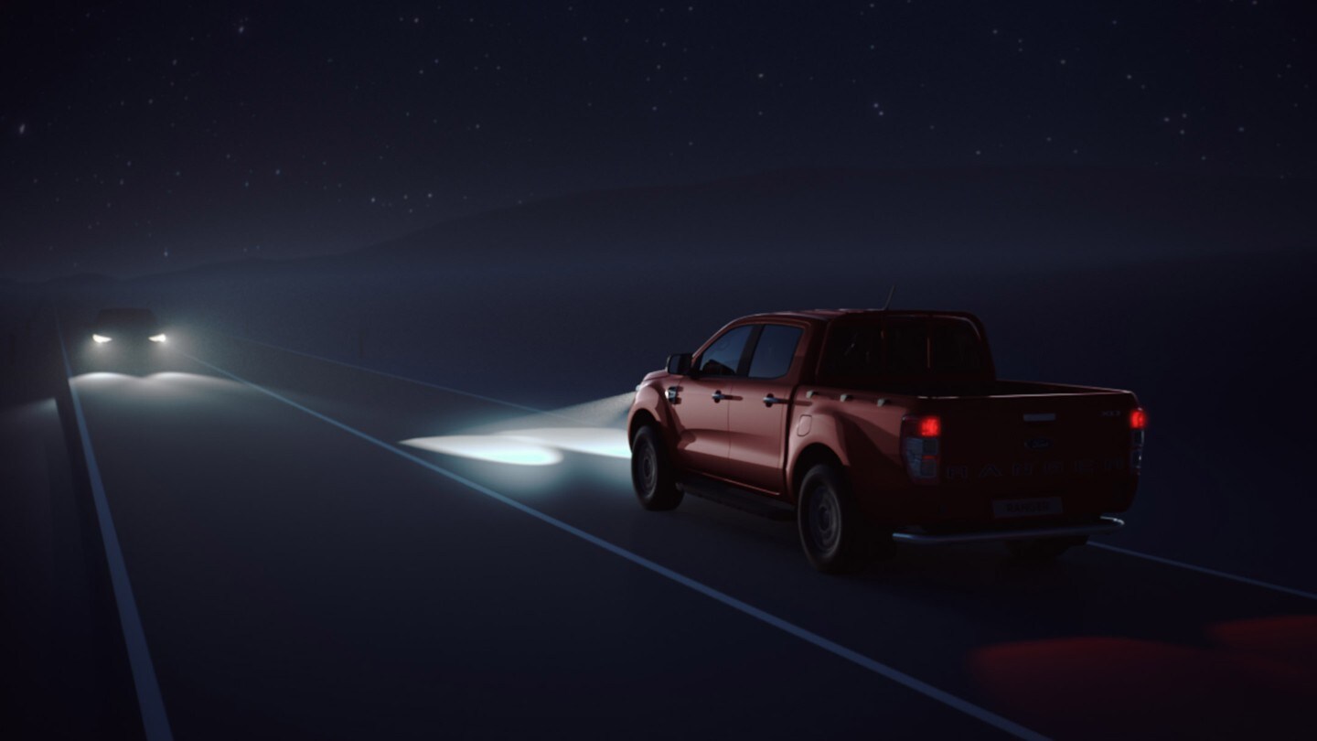 Ford Ranger couleur orange, vue arrière aux trois quarts, roulant de nuit sur une route de campagne
