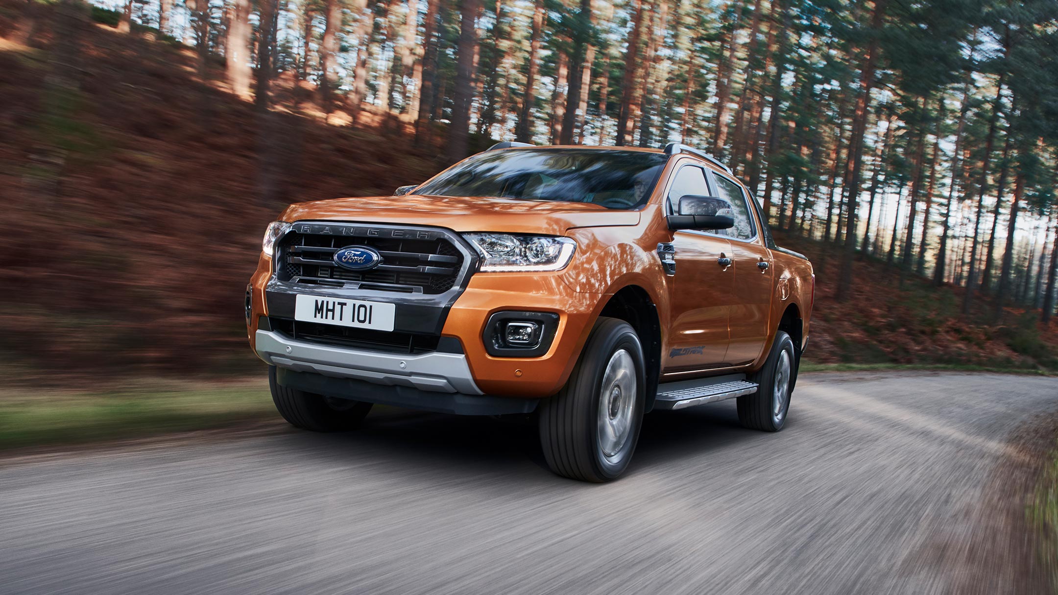 Ford Ranger couleur orange, vue de face aux trois quarts, roulant sur une route de forêt
