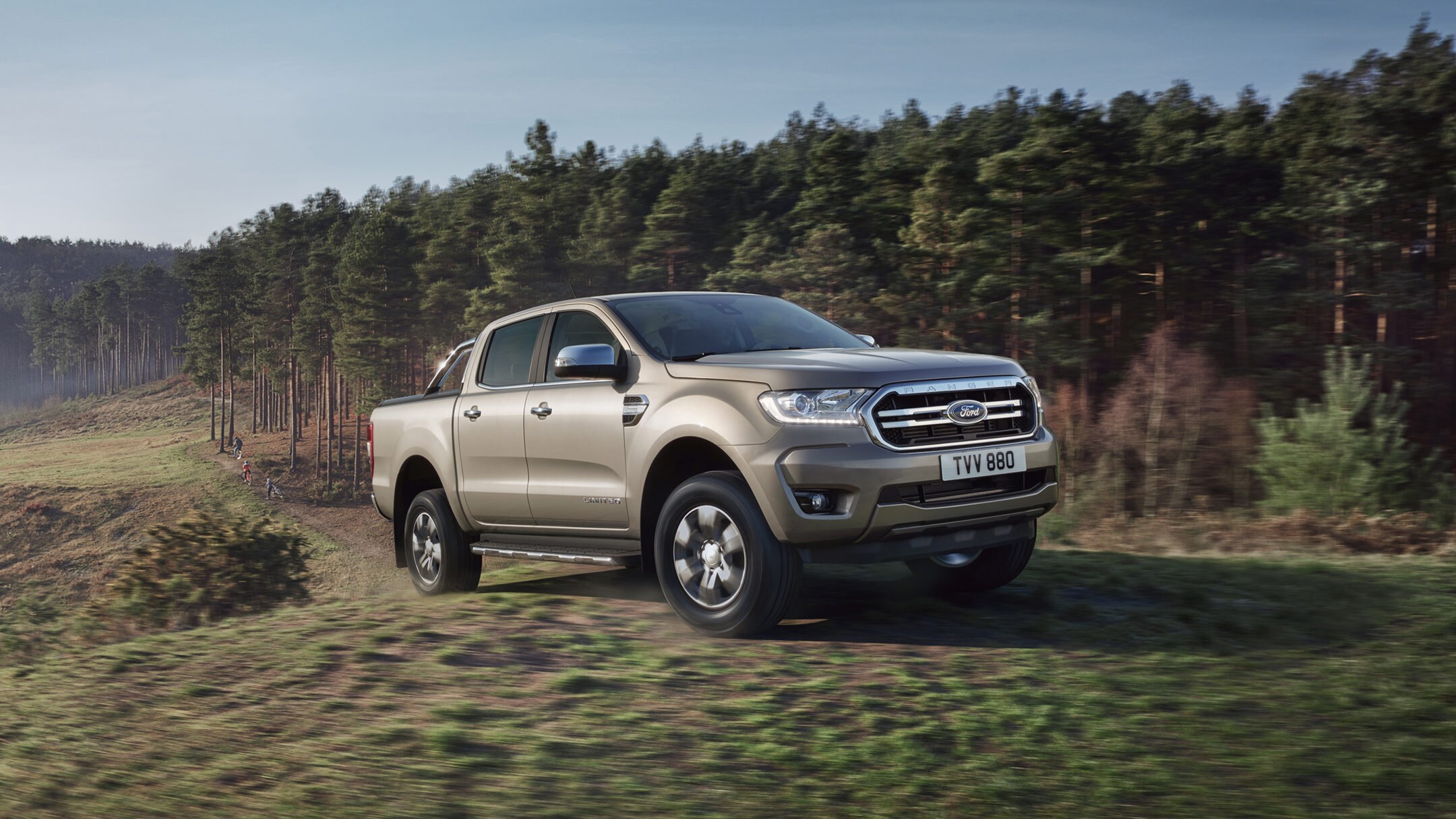 Ford Ranger couleur argent, vue de face aux trois quarts, roulant sur une prairie près d’une forêt
