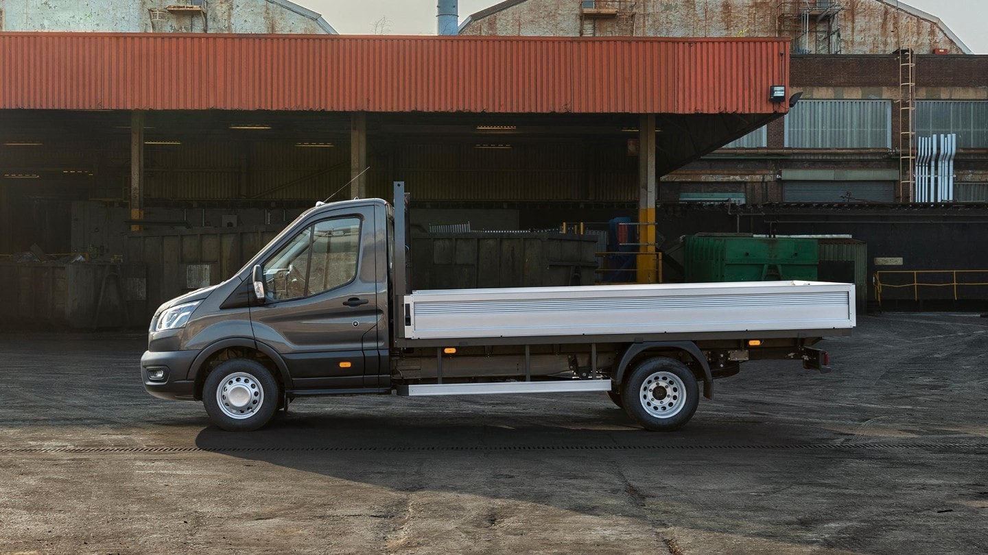 Vue latérale sur un Ford Transit Chassis Cab de 5 tonnes noir garé sur aire d’entreprise à côté d’un abri avec palettes