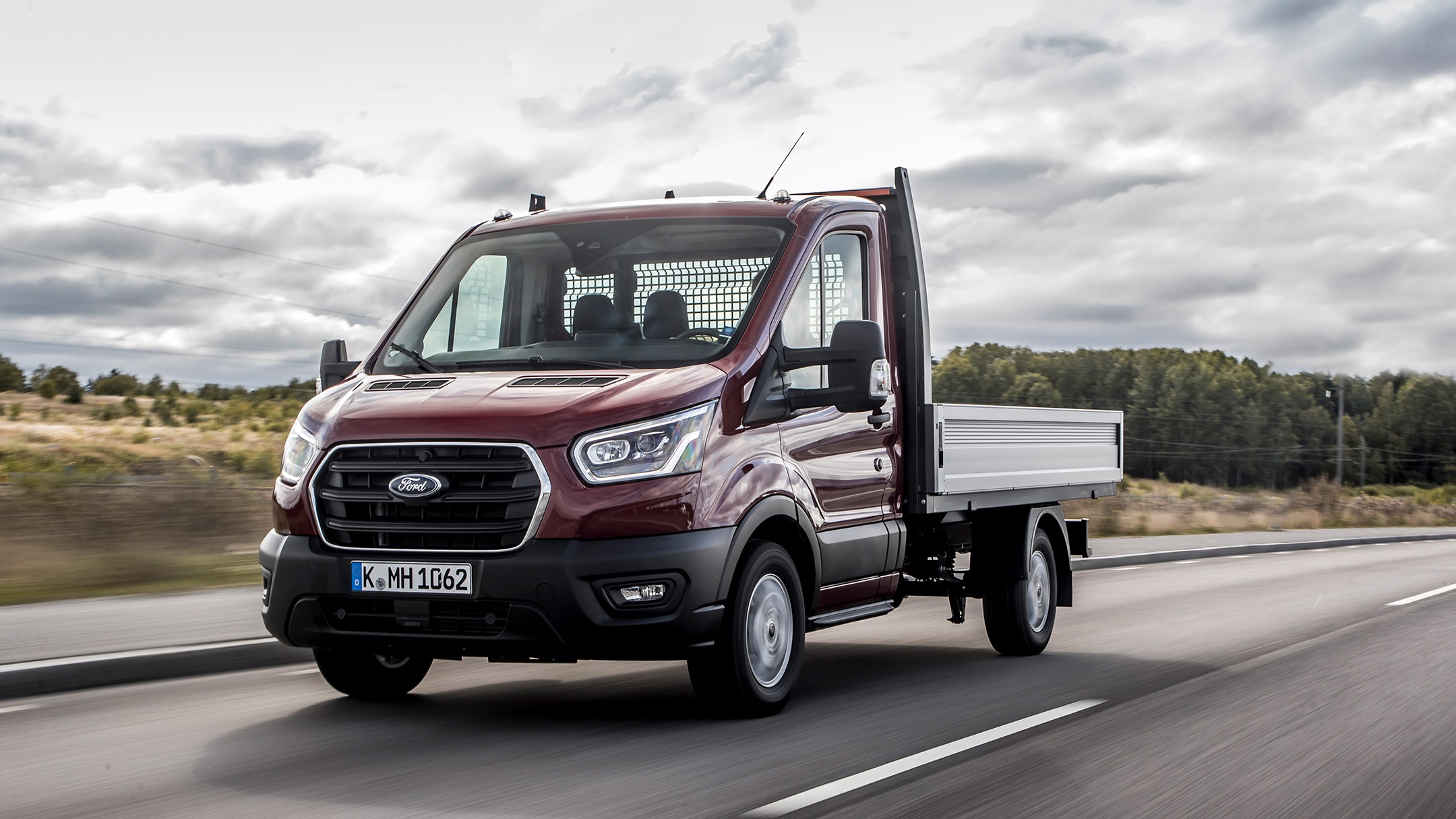 Ford Transit Plateau cabine couleur rouge, vue de face aux trois quarts, roulant sur une route de campagne