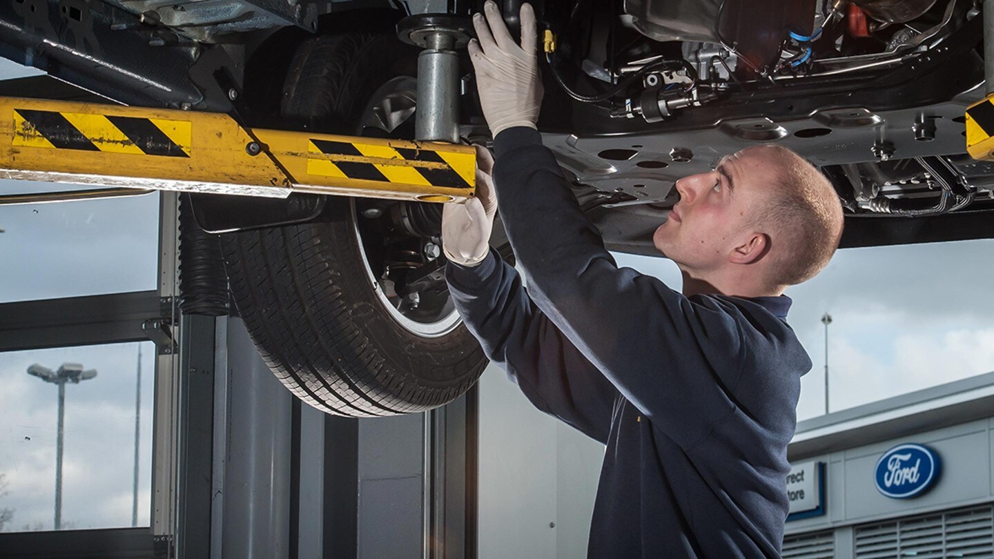 Un homme travaille sur un véhicule sous une plateforme dans un garage Ford