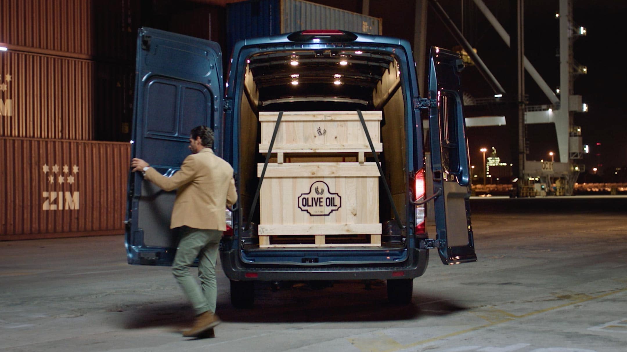 Ford Transit Fourgon couleur bleue, vue arrière, portes arrière ouvertes, stationnant devant des conteneurs.