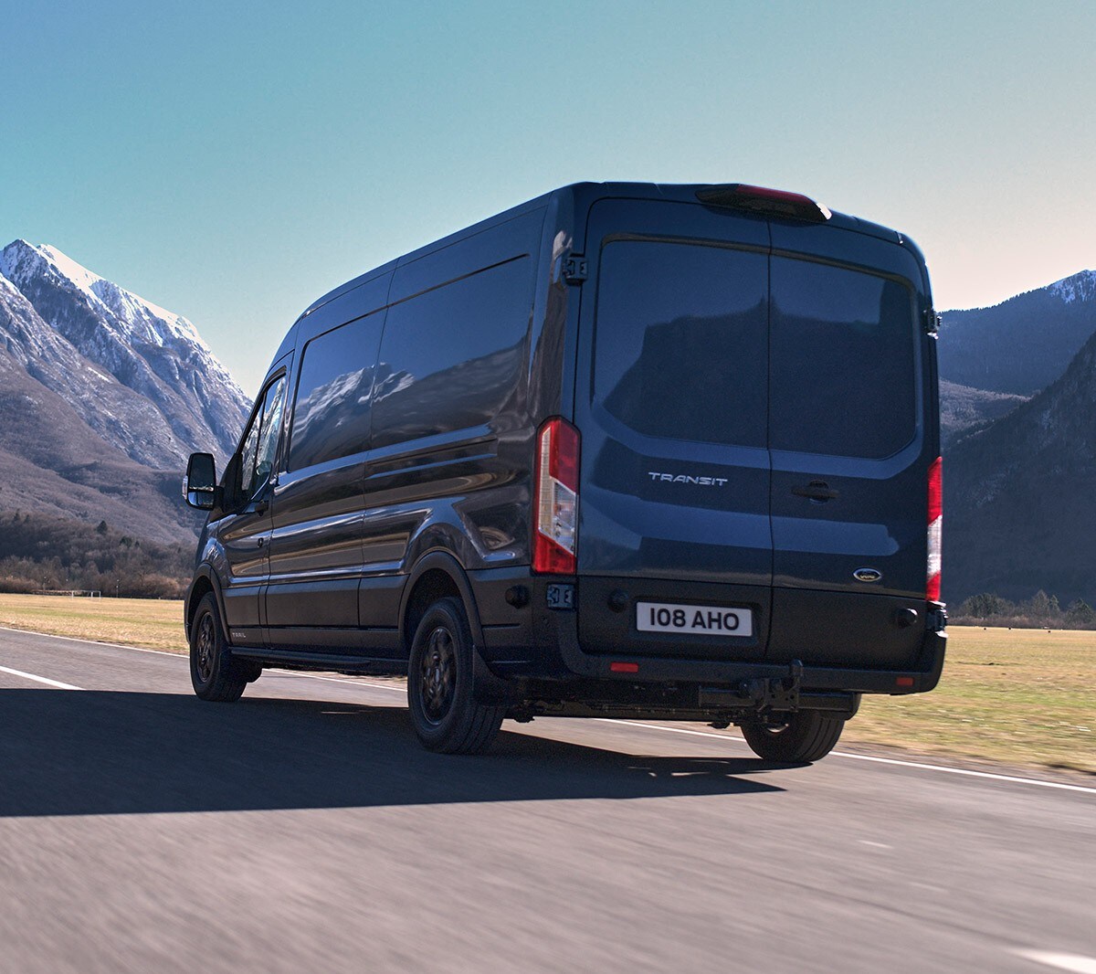 Fourgon Ford Transit bleu. Vue ¾ arrière. Conduite à travers le pays