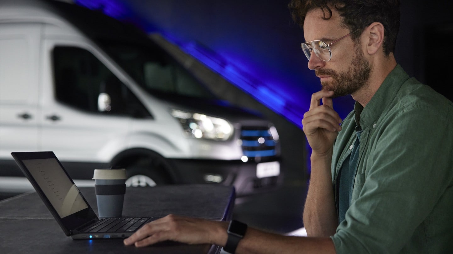 Homme assis à son ordinateur portable avec un Ford E-Transit en arrière-plan 