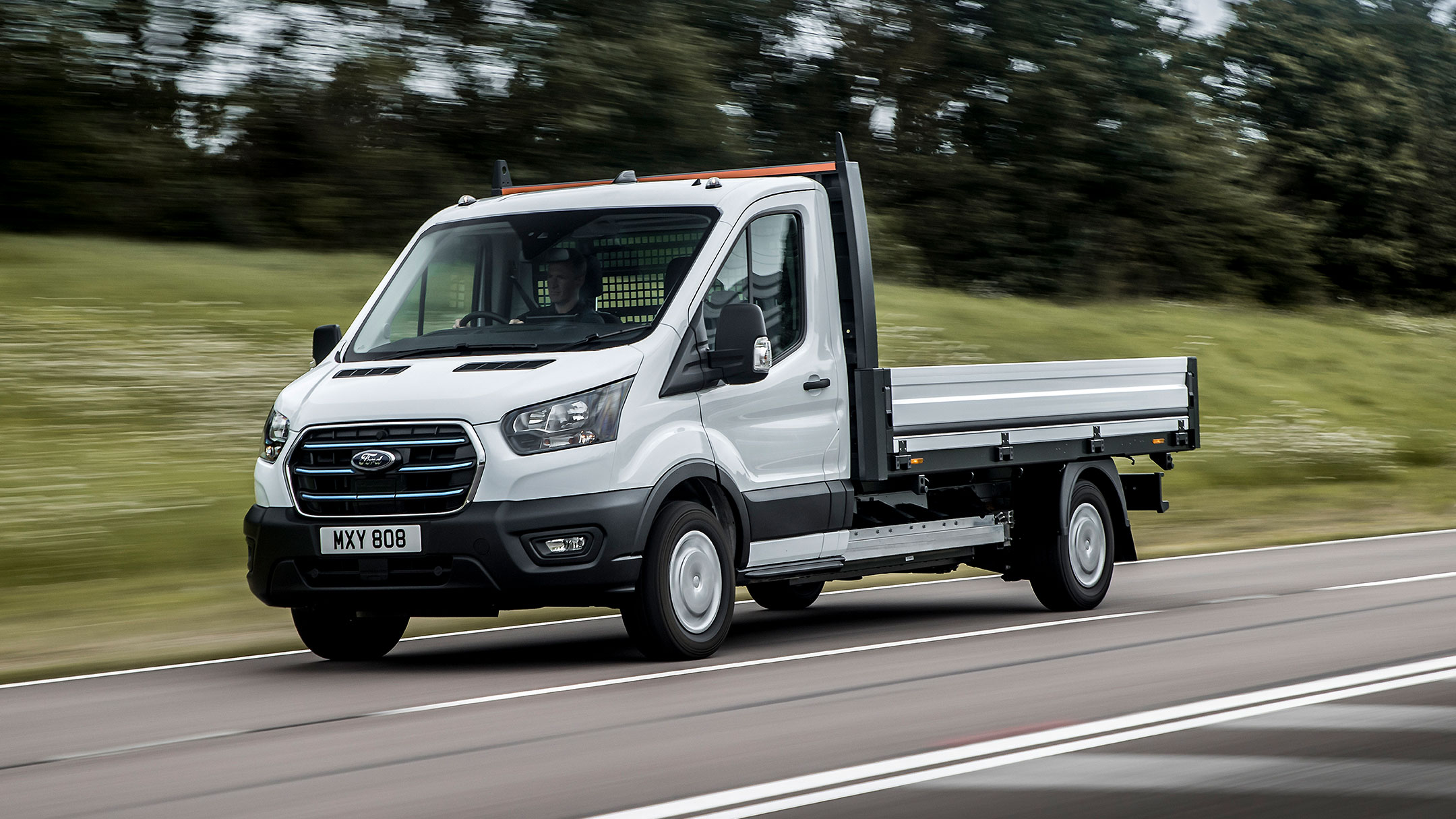 Ford E-Transit Châssis cabine couleur blanche, vue de face aux trois quarts, roulant sur une route de campagne