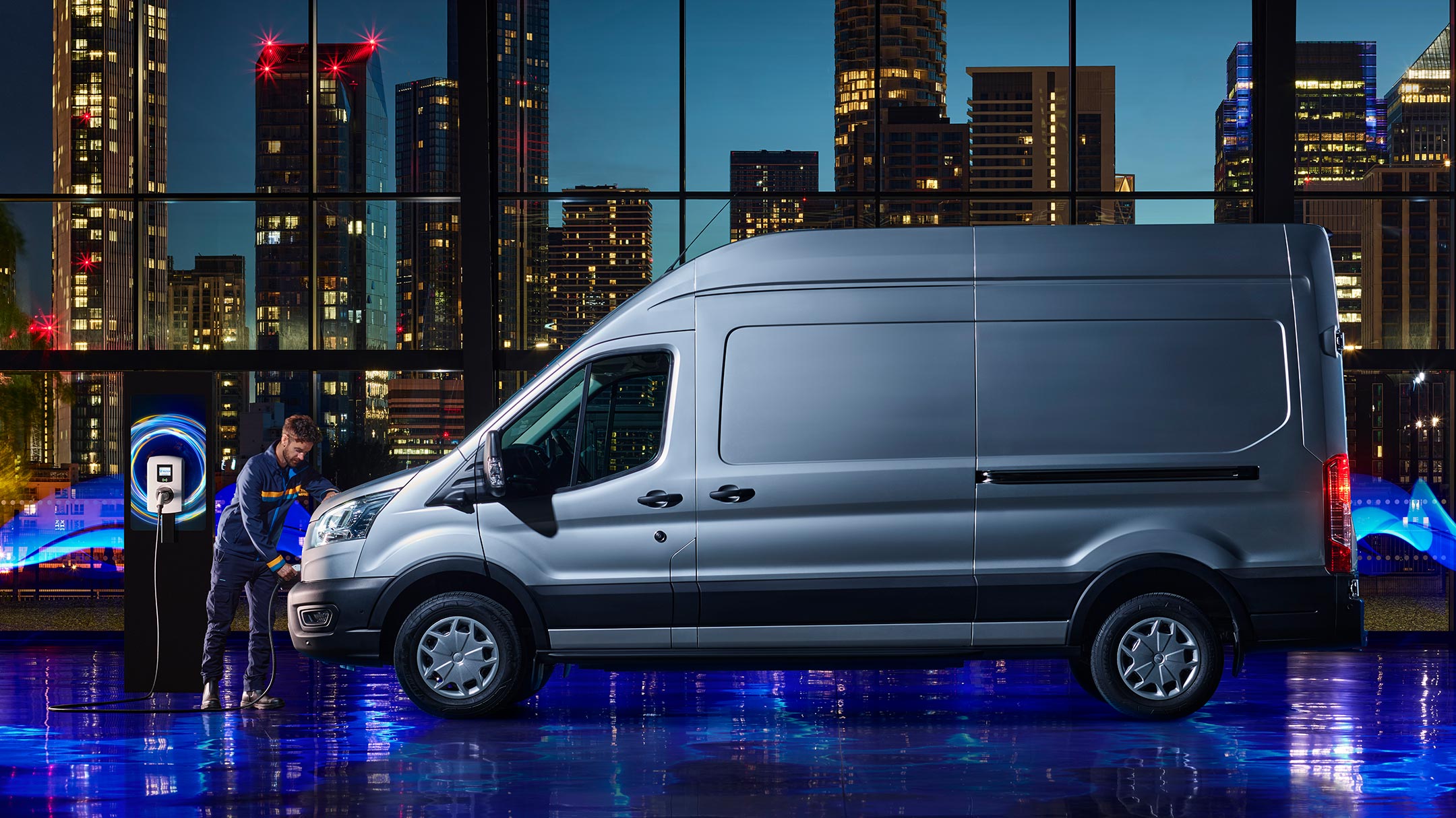 Ford E-Transit couleur argent, vue latérale, garé dans un showroom et en cours de recharge