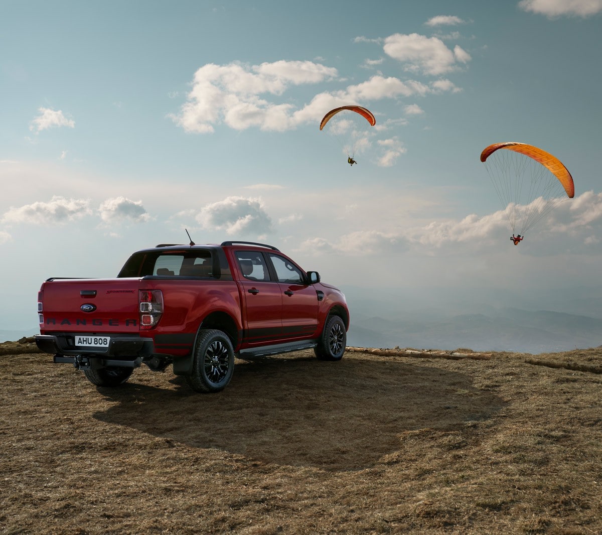 Ford Ranger Stormtrak rouge, vue de profil aux trois quarts, garé dans un paysage de dunes avec un parapente dans le ciel