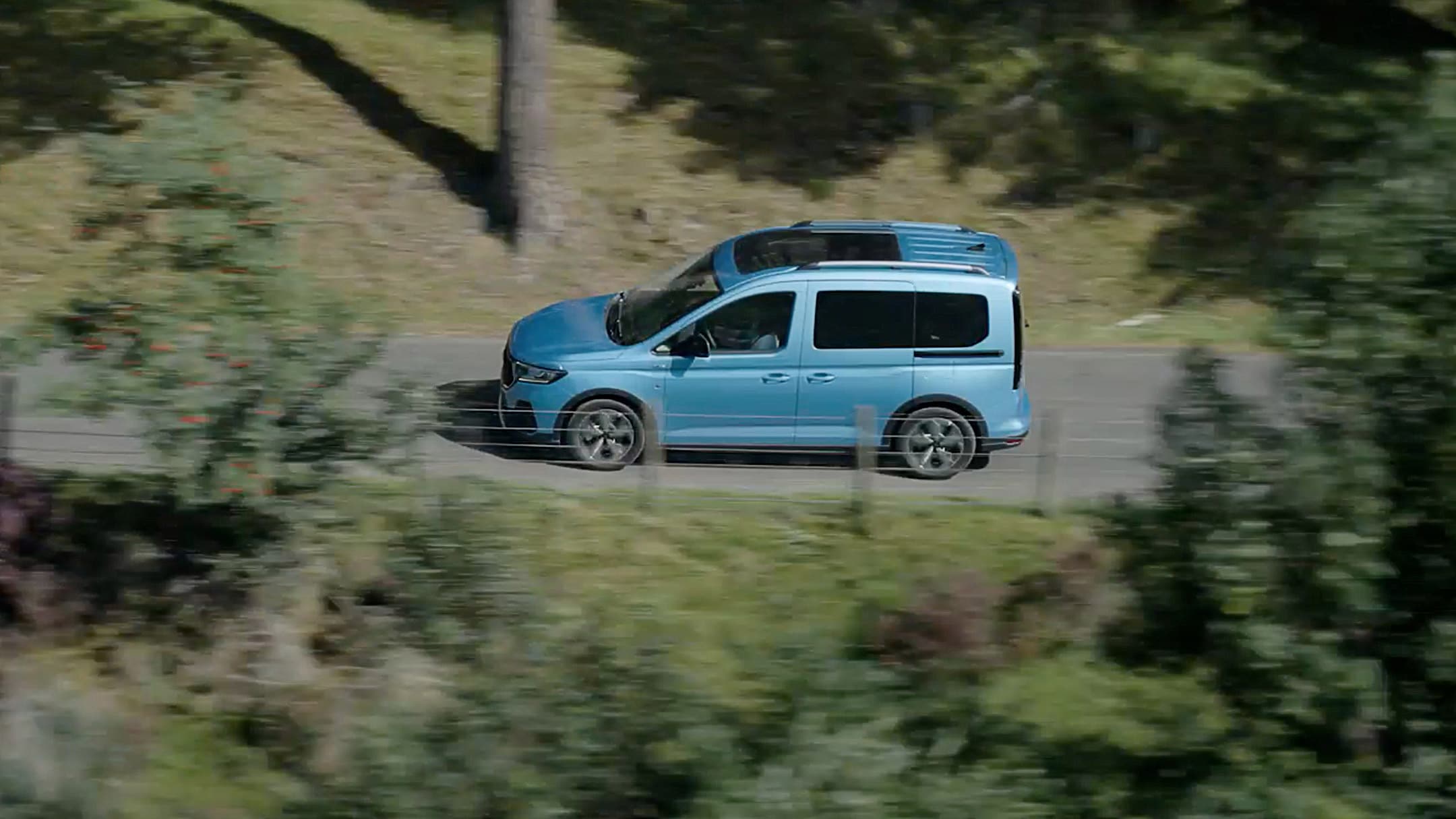 Ford Tourneo Connect couleur bleu clair, vue latérale aérienne, roulant sur une route de campagne