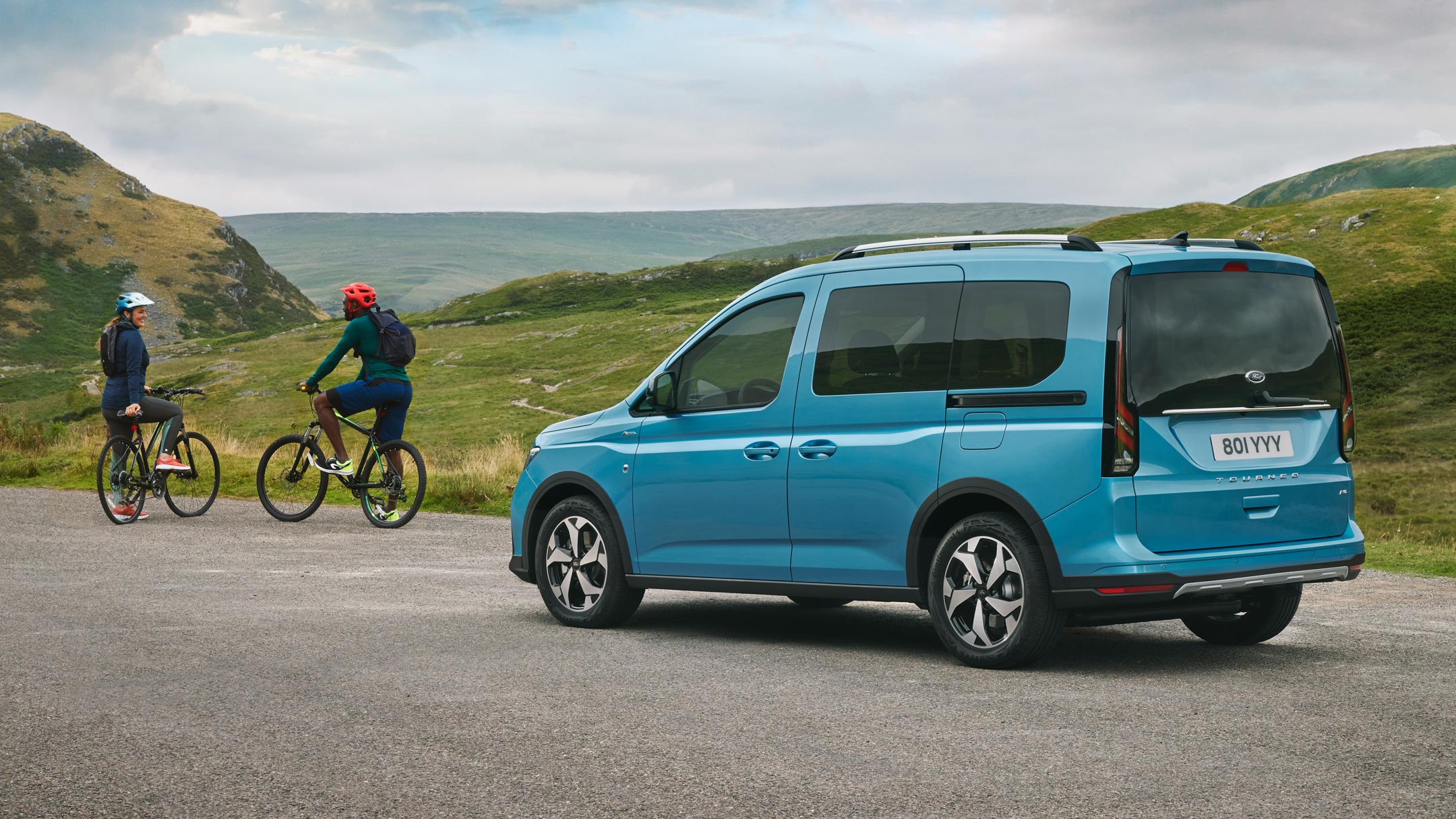 Ford Tourneo Connect couleur bleu clair, vue arrière aux trois quarts, sur une route de campagne, précédé de deux cyclistes