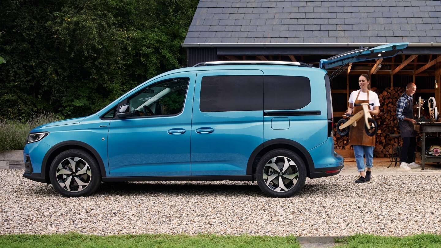 Ford Tourneo Connect couleur bleu clair, vue latérale avec hayon ouvert. Femme remplissant le coffre