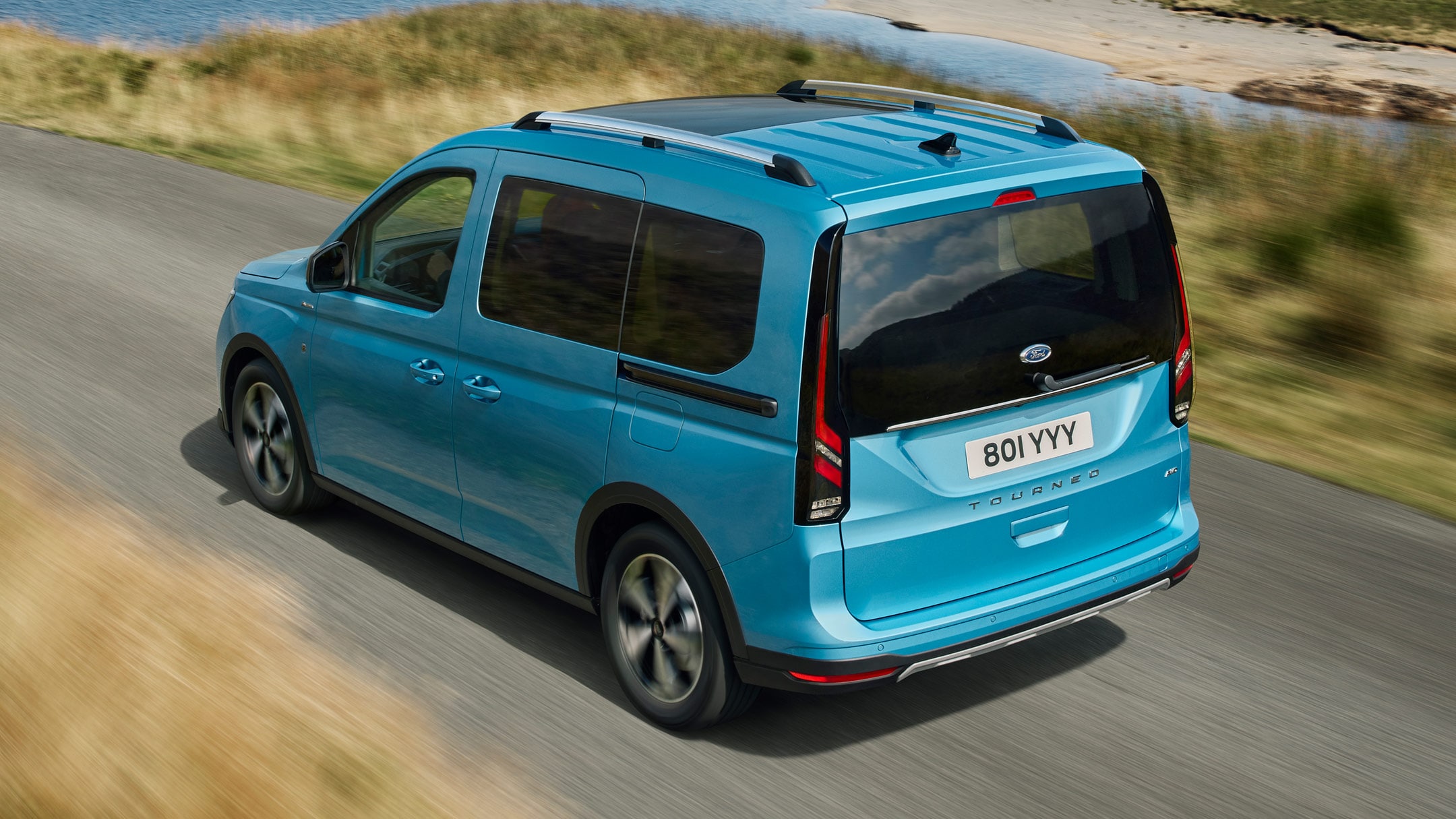 Ford Tourneo Connect couleur bleu clair, vue arrière aux trois quarts, roulant sur une route de campagne