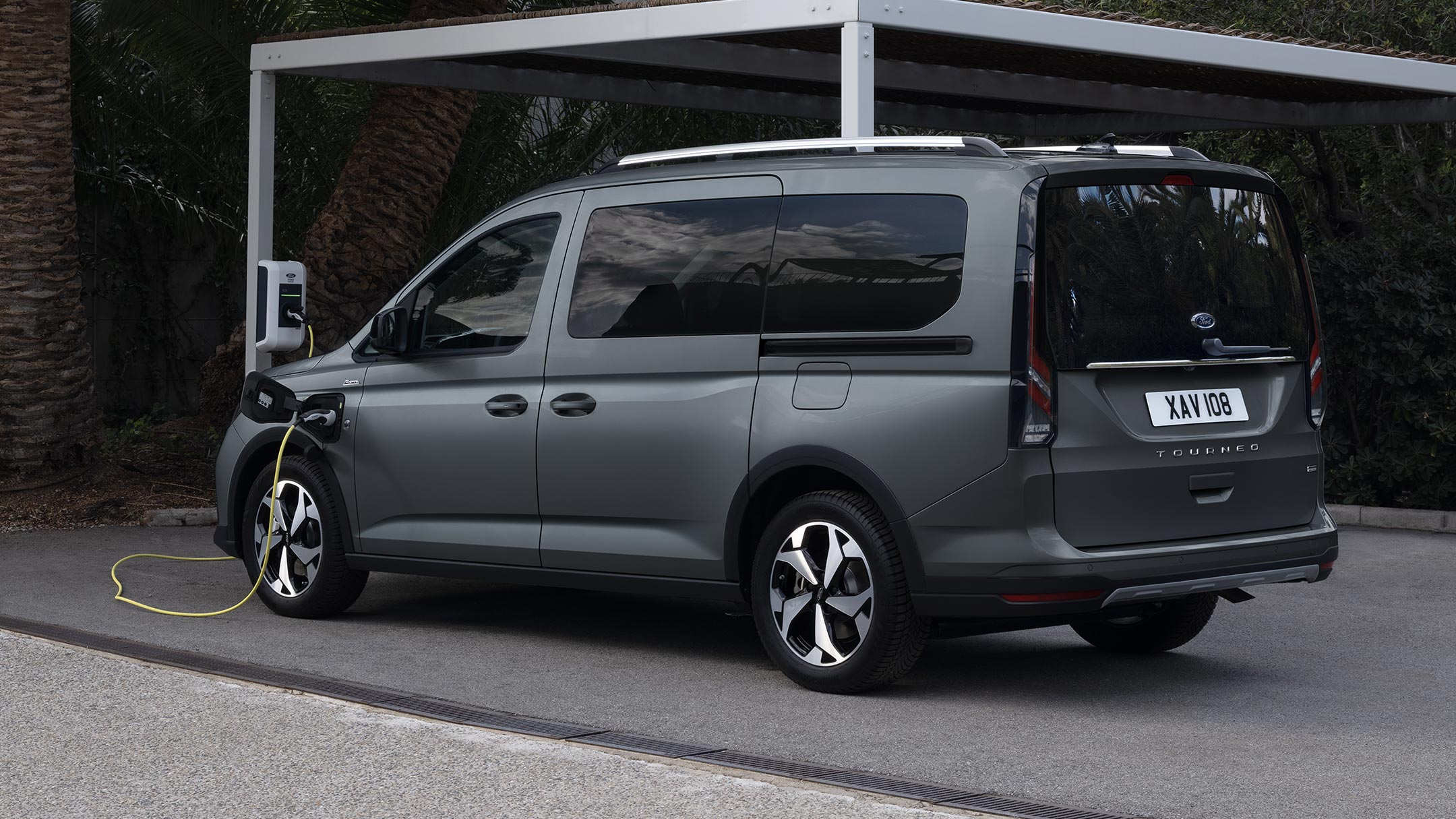 Ford Tourneo Connect couleur grise, vue de face aux trois quarts, stationnant devant un paysage montagneux avec rivière en arrière-plan