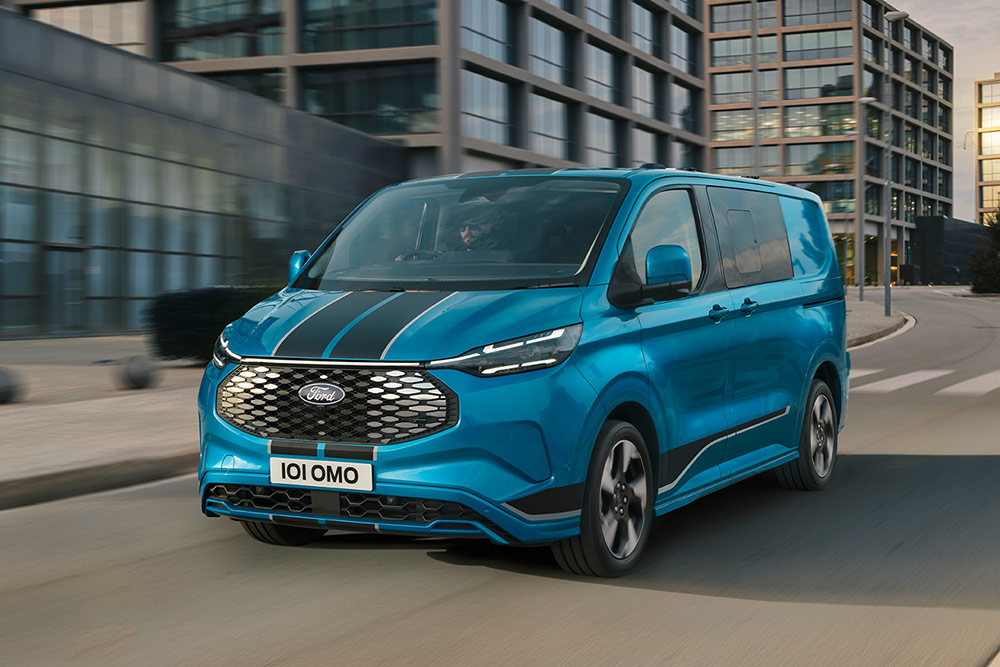 Camionnette Ford E-Transit Custom Sport double cabine bleue circulant dans une rue de la ville.