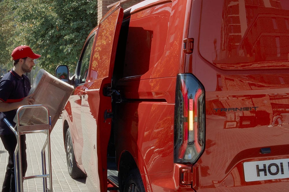 Un livreur décharge des colis d'un Ford Transit Custom rouge.
