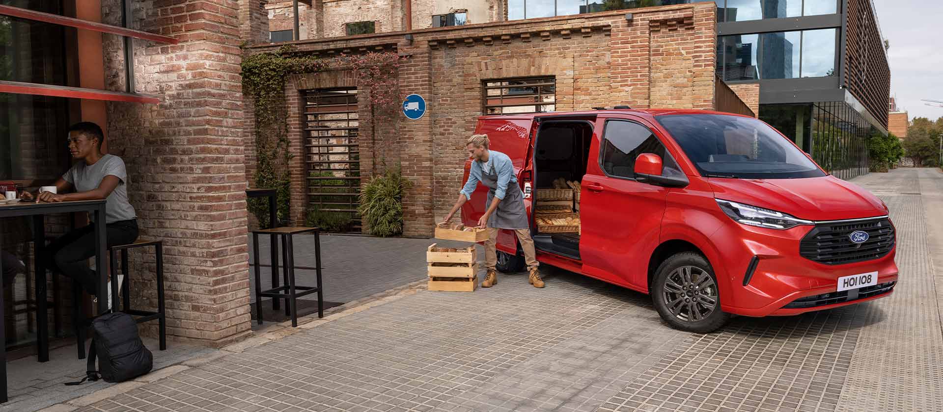 Fourgon Ford Transit Custom rouge garé devant un café.