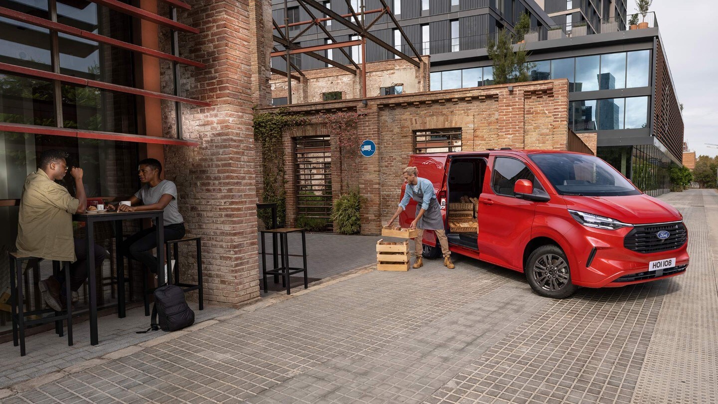 Ford Transit Custom couleur rouge, vue de face aux trois quarts, en train d’être déchargé devant un restaurant