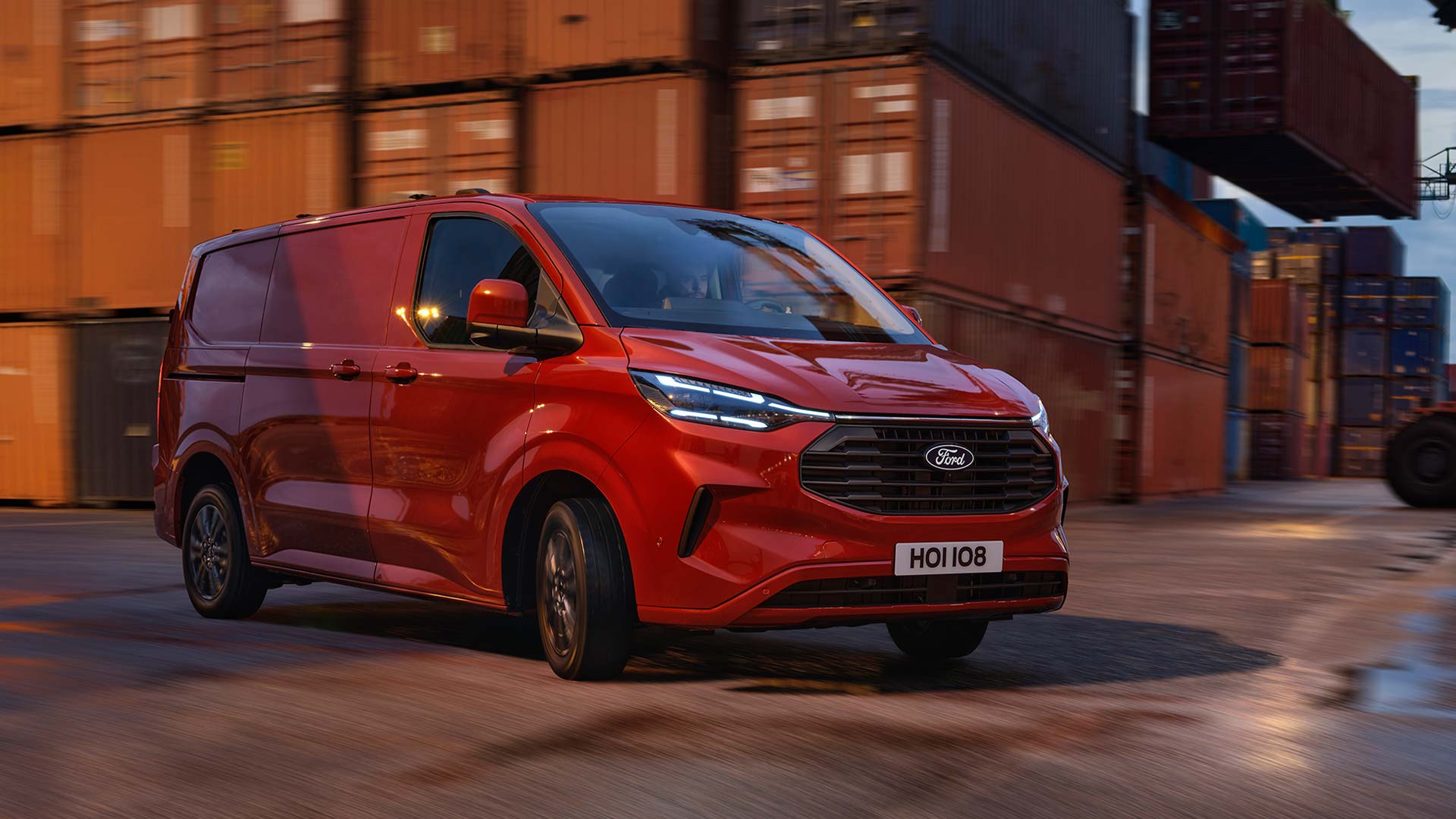 Une camionnette Ford Transit Custom rouge circule dans une zone portuaire.