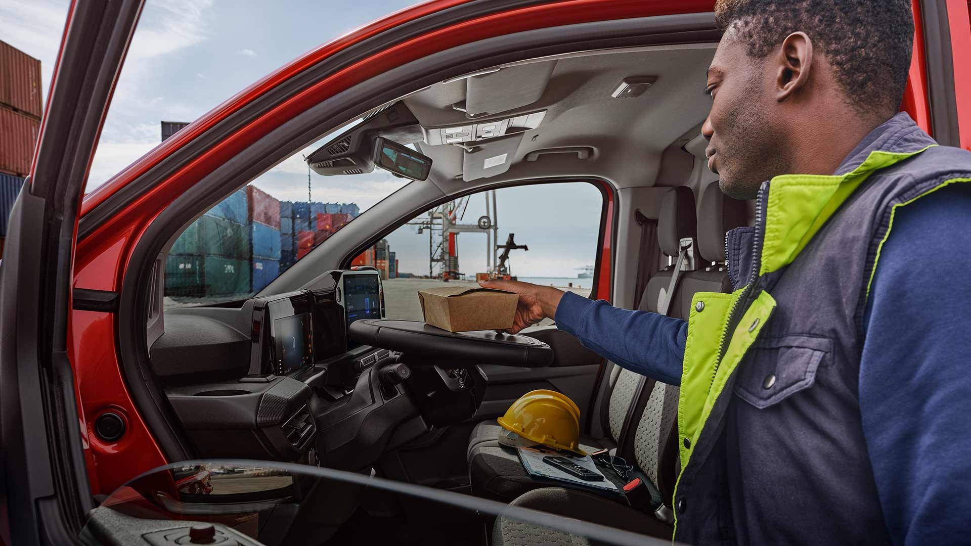 Une personne dépose un colis dans une Ford Transit Custom rouge.